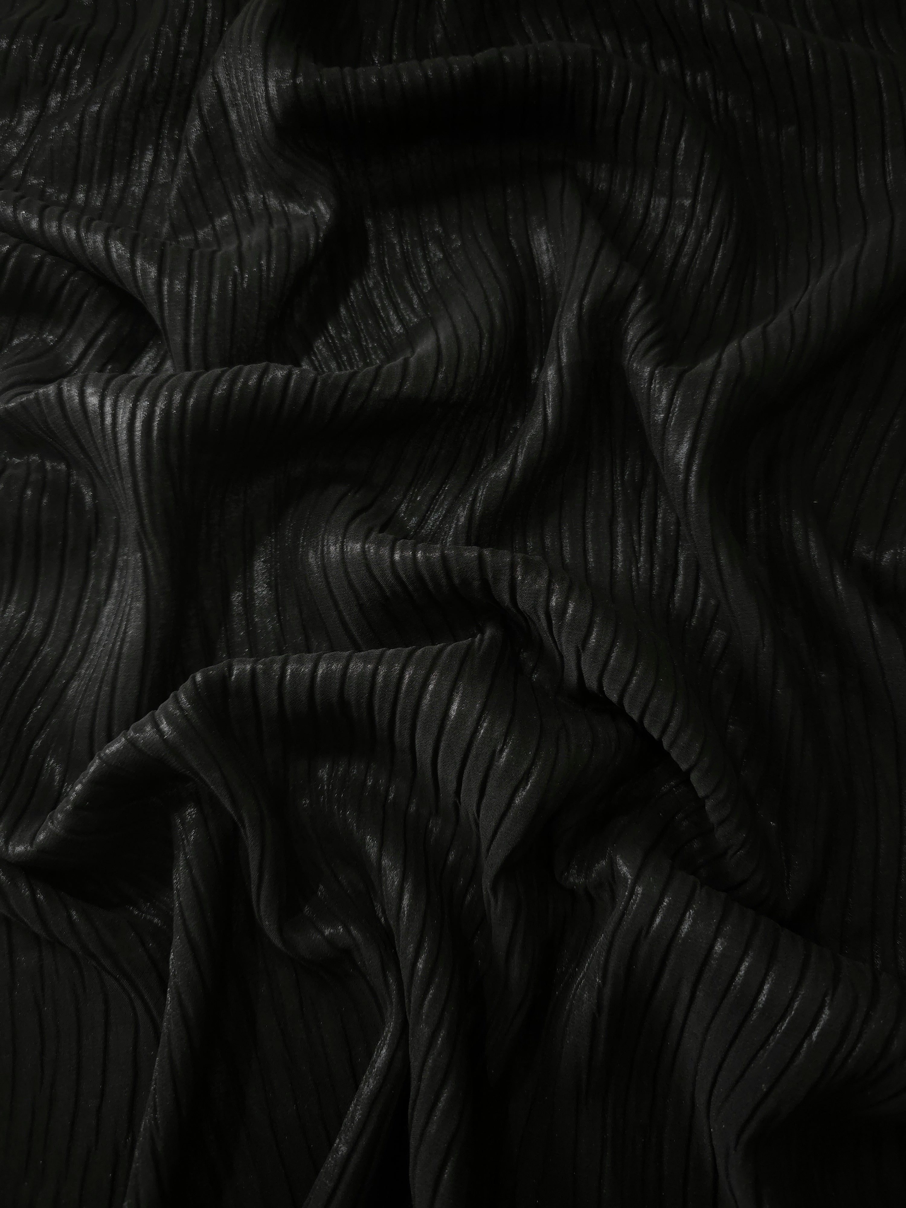 Flowing drape of Jet Black classic plissé shimmer fabric, showing regular pleated texture and light-catching movement for evening gowns and flowing maxi skirts.