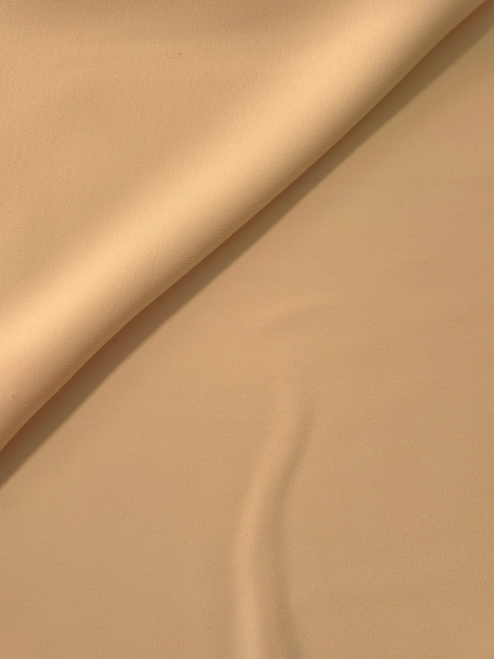 Soft fold of Camel Beige opaque polyester crepe showing fluid dressmaking drape for dresses and skirts