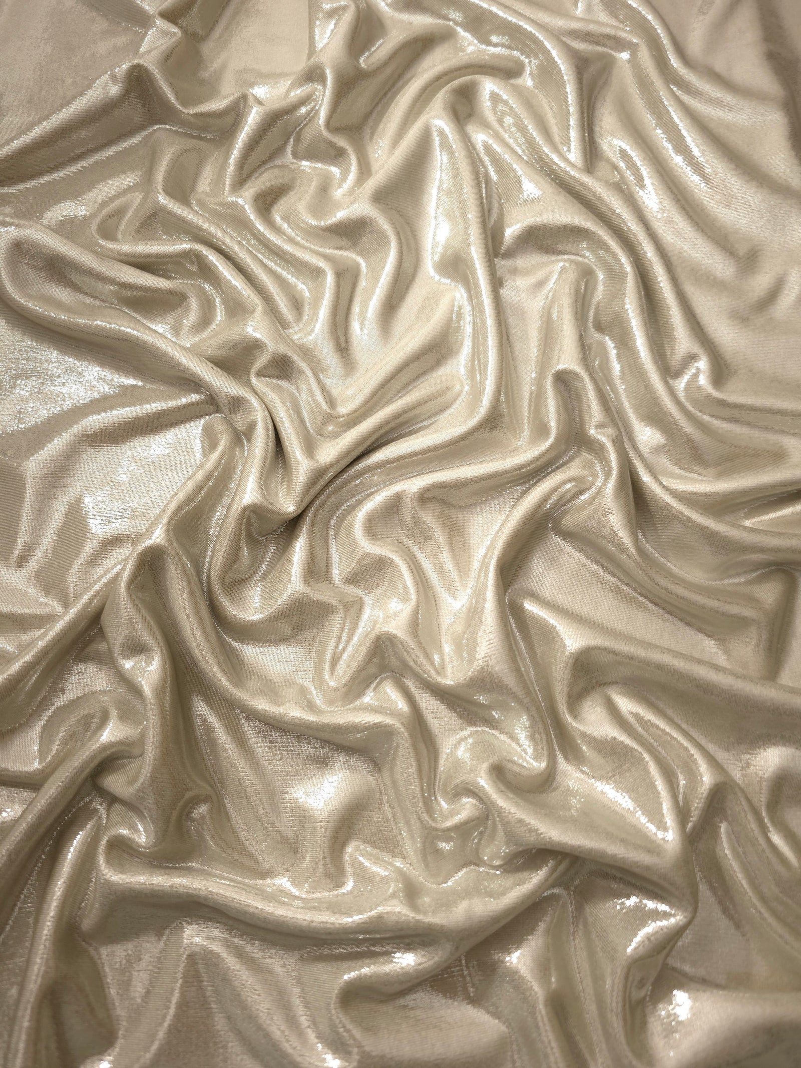 Champagne Beige metallic stretch fabric arranged in elegant folds, showing reflective movement for occasionwear, costumes and fashion design