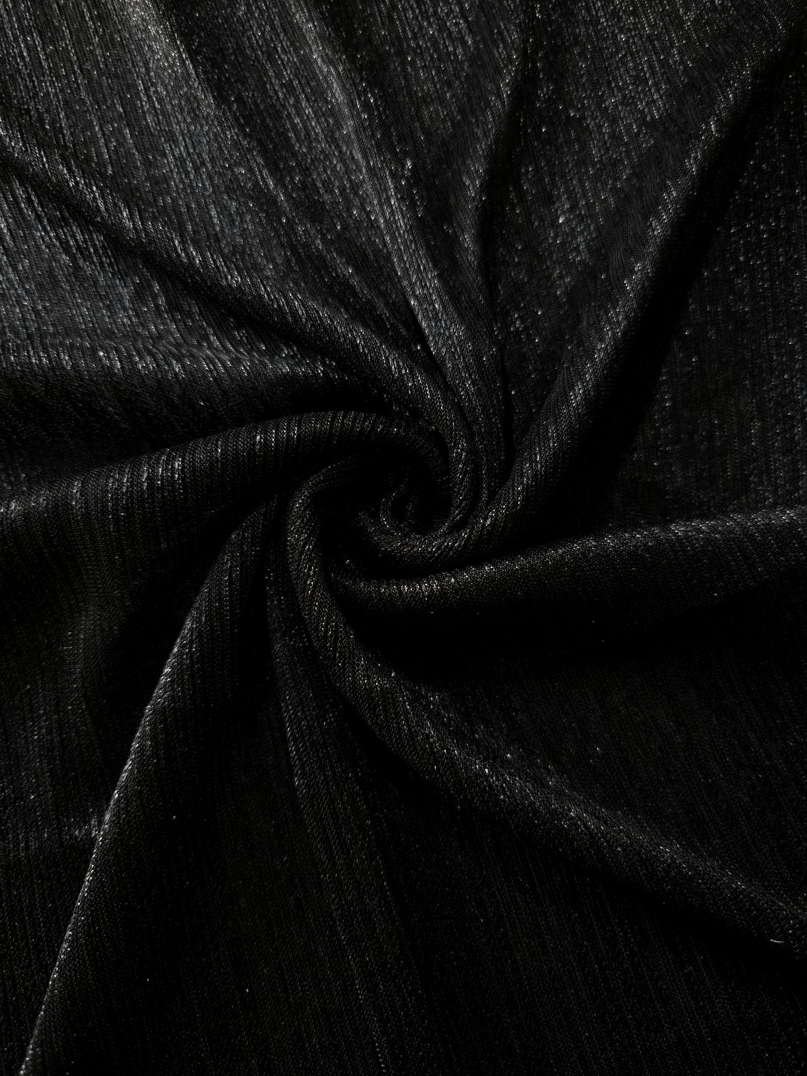 Swirl-draped Charcoal Black Sheer Metallic Shimmer Stretch Tulle Fabric showing fluid movement, reflective shimmer, airy transparency and flexible stretch for dresses, dancewear and stage looks