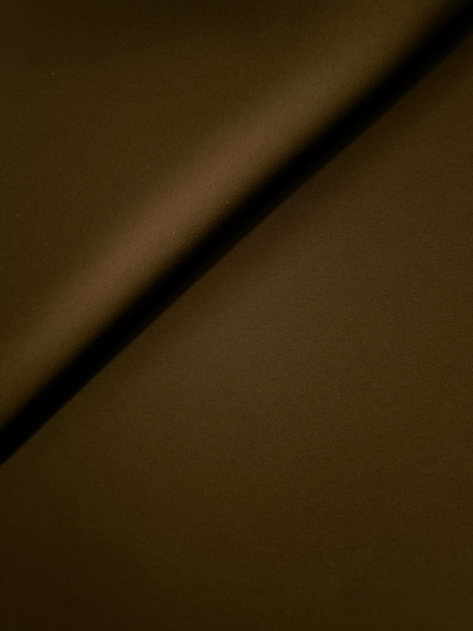 Soft fold of Dark Walnut Brown opaque polyester crepe showing fluid dressmaking drape for dresses and skirts