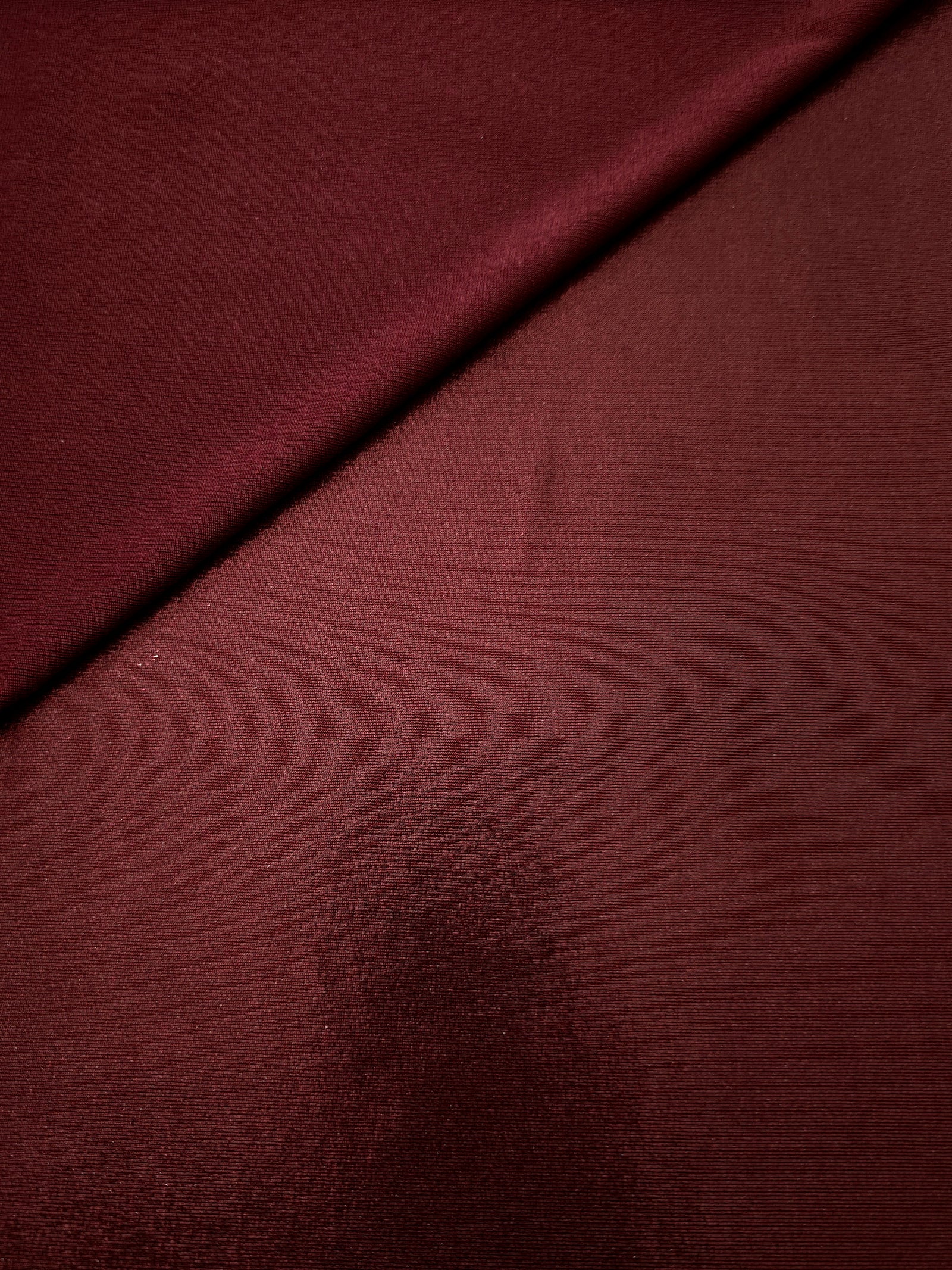 Gently folded Deep Burgundy shimmer spandex fabric showing luminous foil finish for tops, skirts and occasion garments