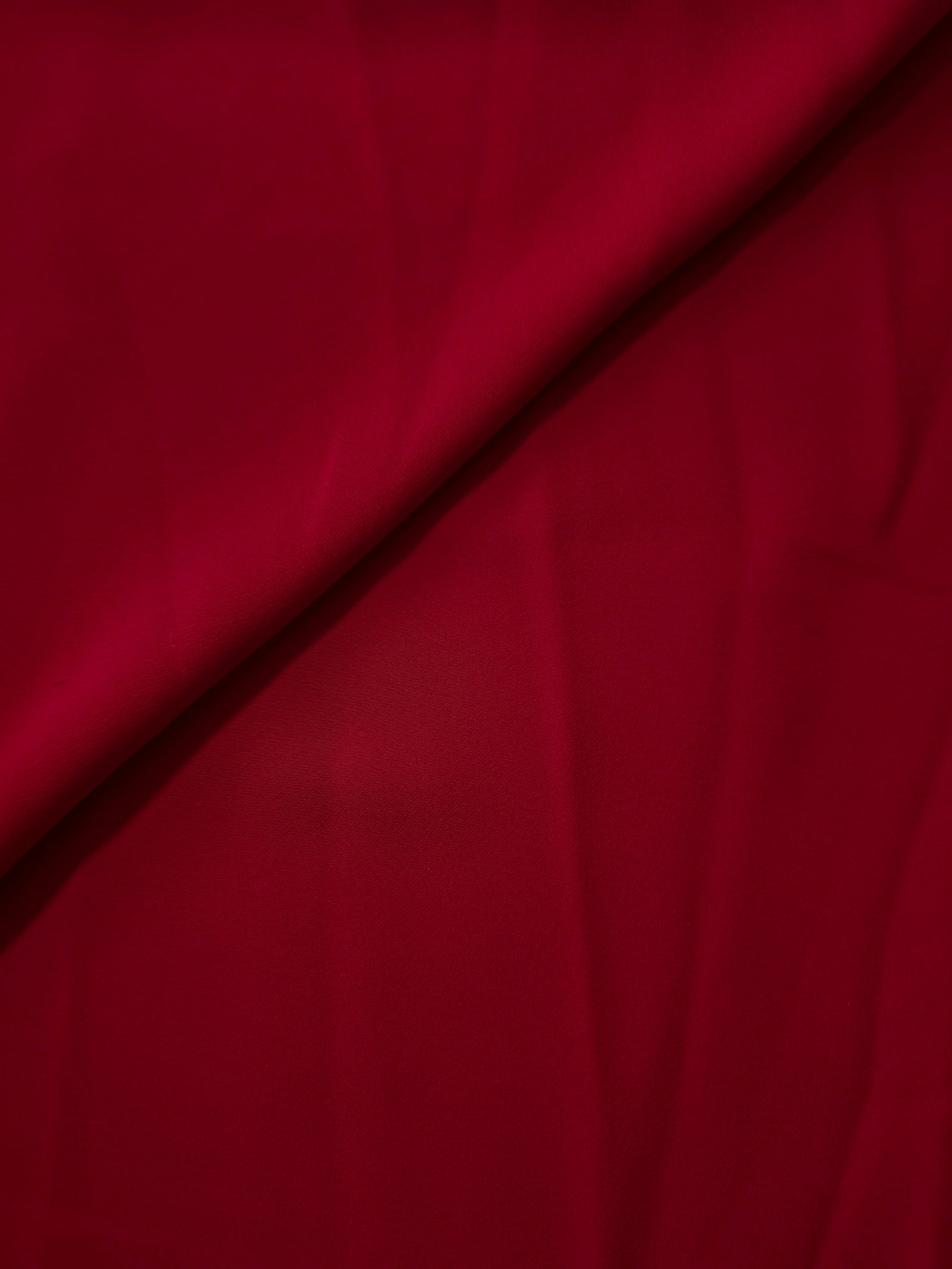 Soft fold of Deep Cherry Red opaque polyester crepe showing fluid dressmaking drape for dresses and skirts