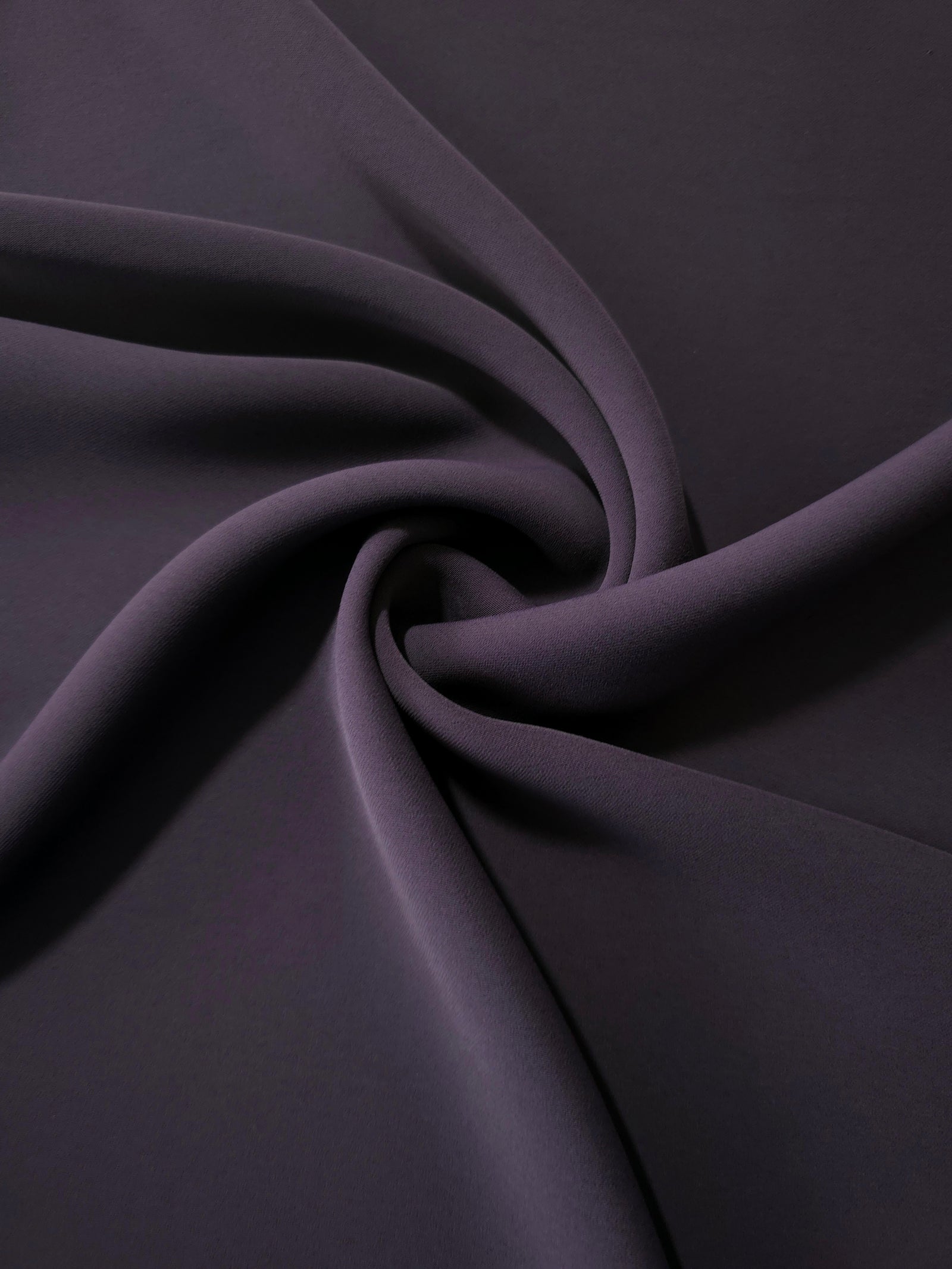 Flowing swirl of Deep Eggplant Purple Korean polyester crepe showing soft drape for blouses, dresses and abayas