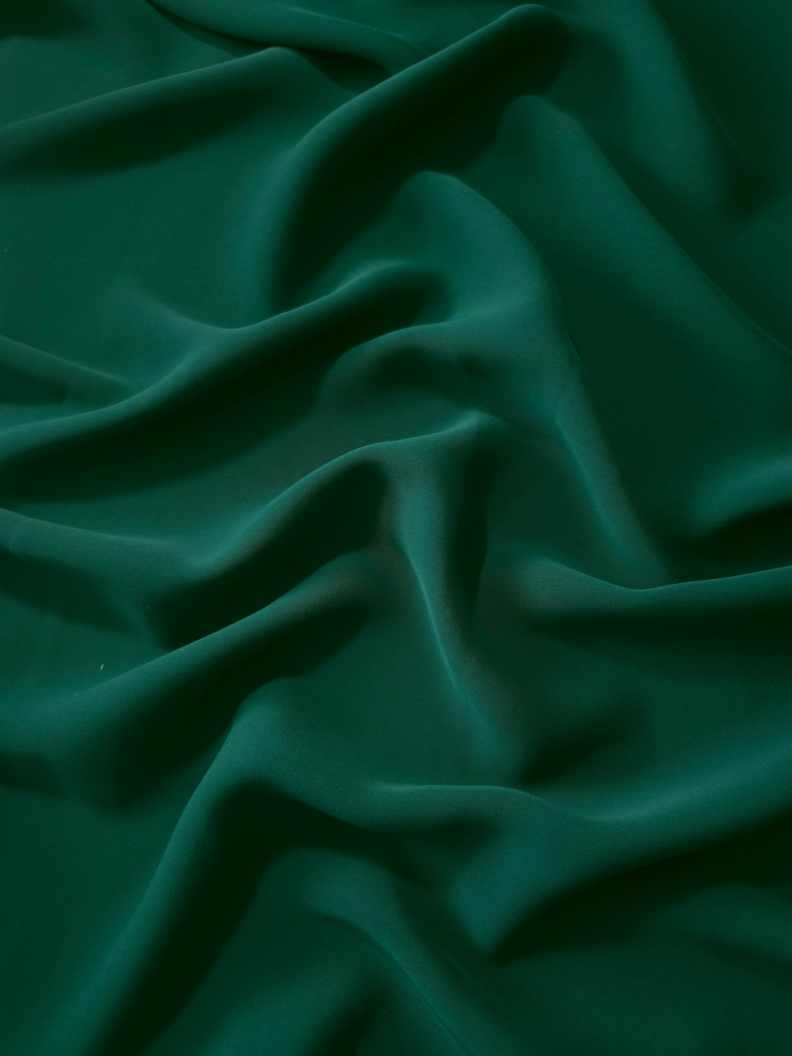Draped folds of Deep Emerald Green polyester crepe showing opaque coverage and fluid movement for garment making