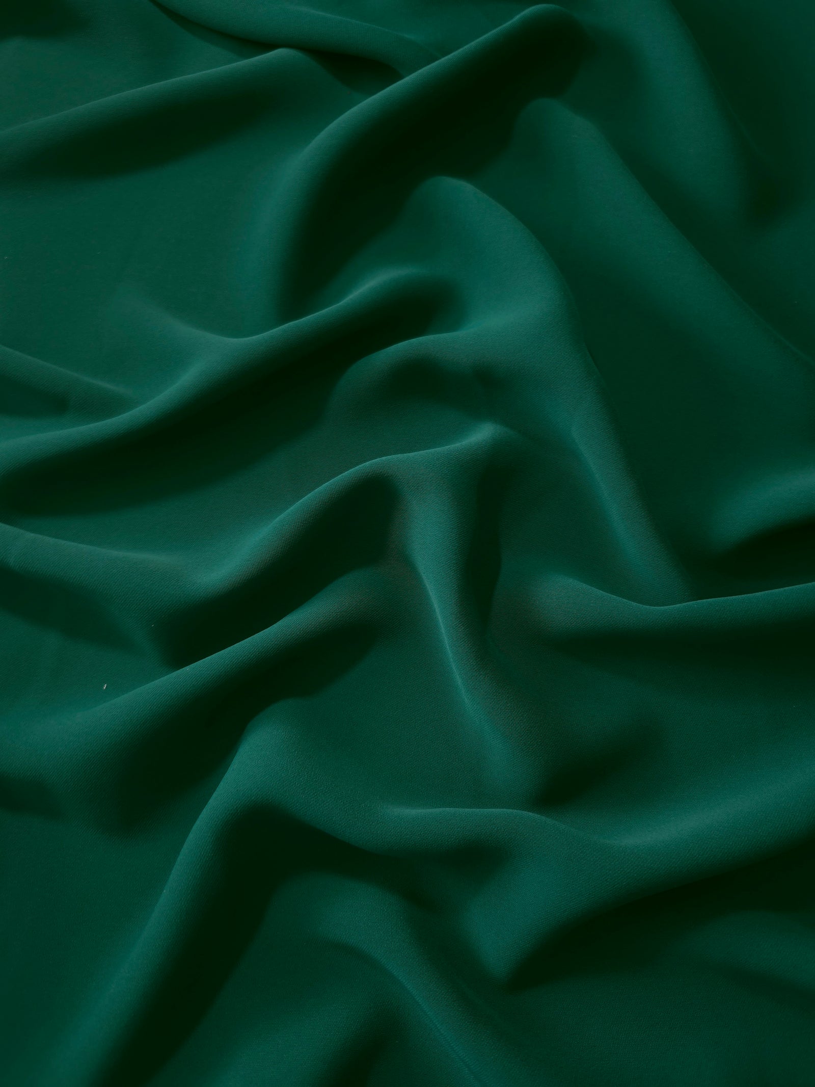 Draped folds of Deep Emerald Green polyester crepe showing opaque coverage and fluid movement for garment making