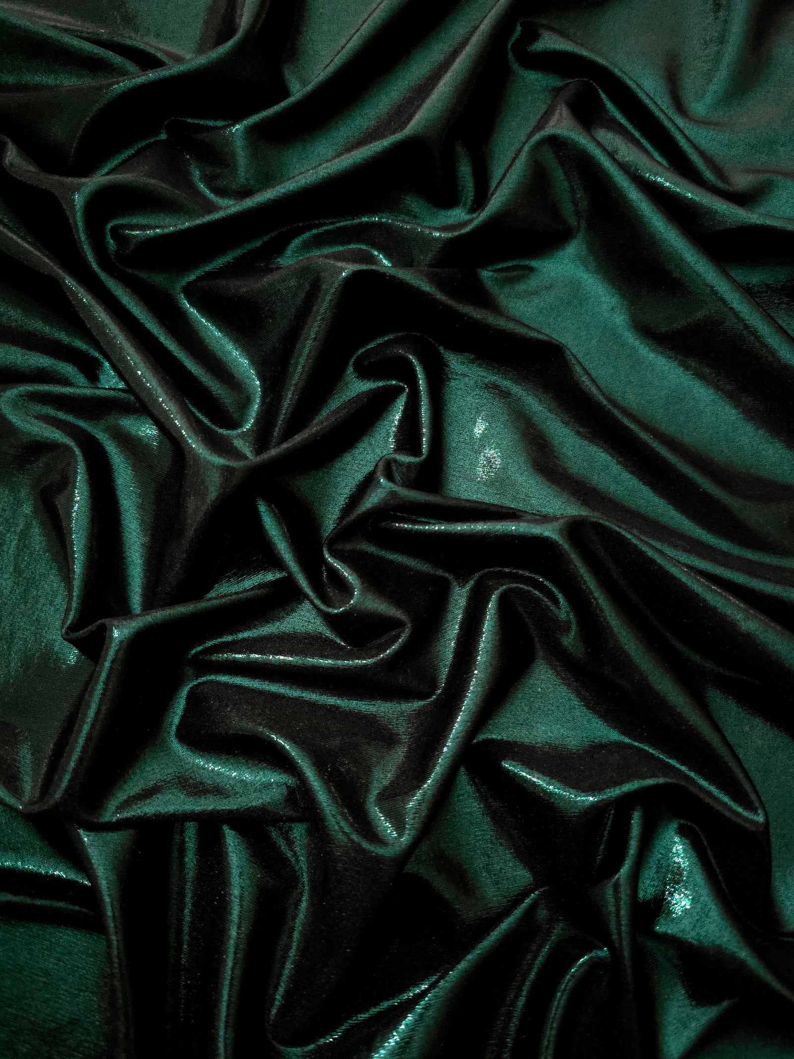 Deep Emerald Green shimmer stretch fabric in draped folds, highlighting metallic foil sheen for evening dresses, costumes and statement apparel