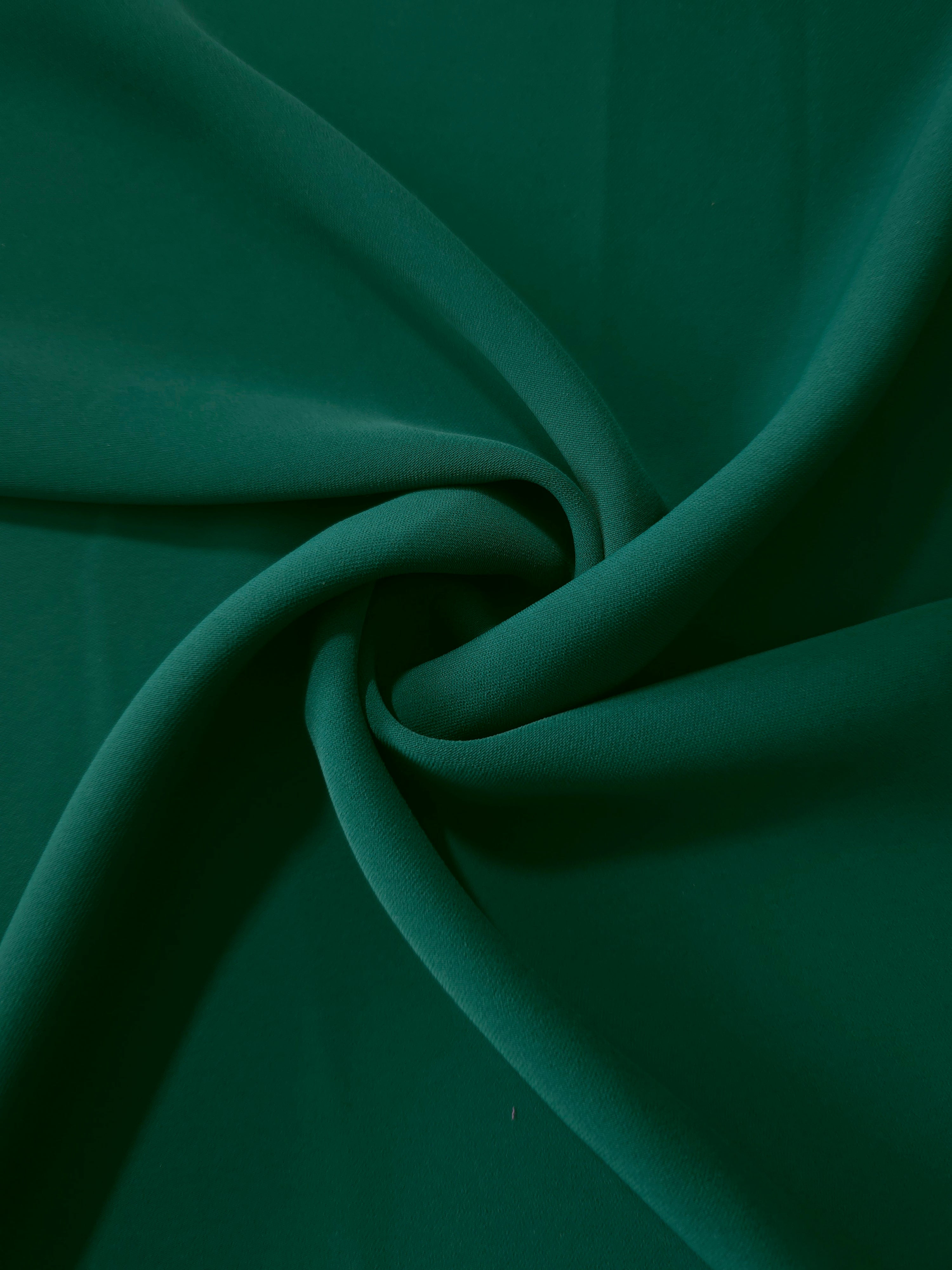 Deep Emerald Green silky-soft polyester crepe styled in a swirl to show fluid dressmaking drape and movement