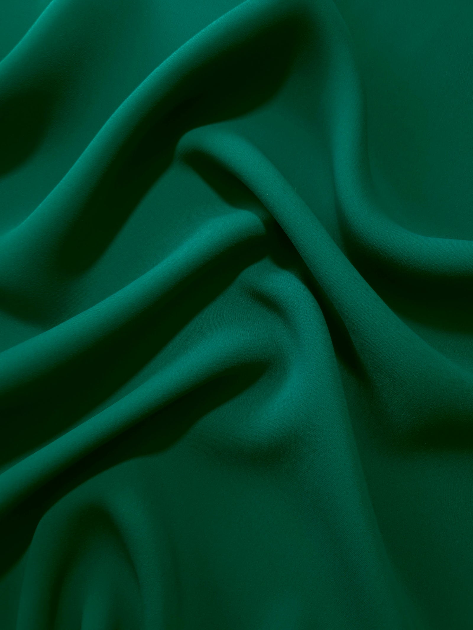 Draped folds of Deep Jade Green polyester crepe showing opaque coverage and fluid movement for garment making