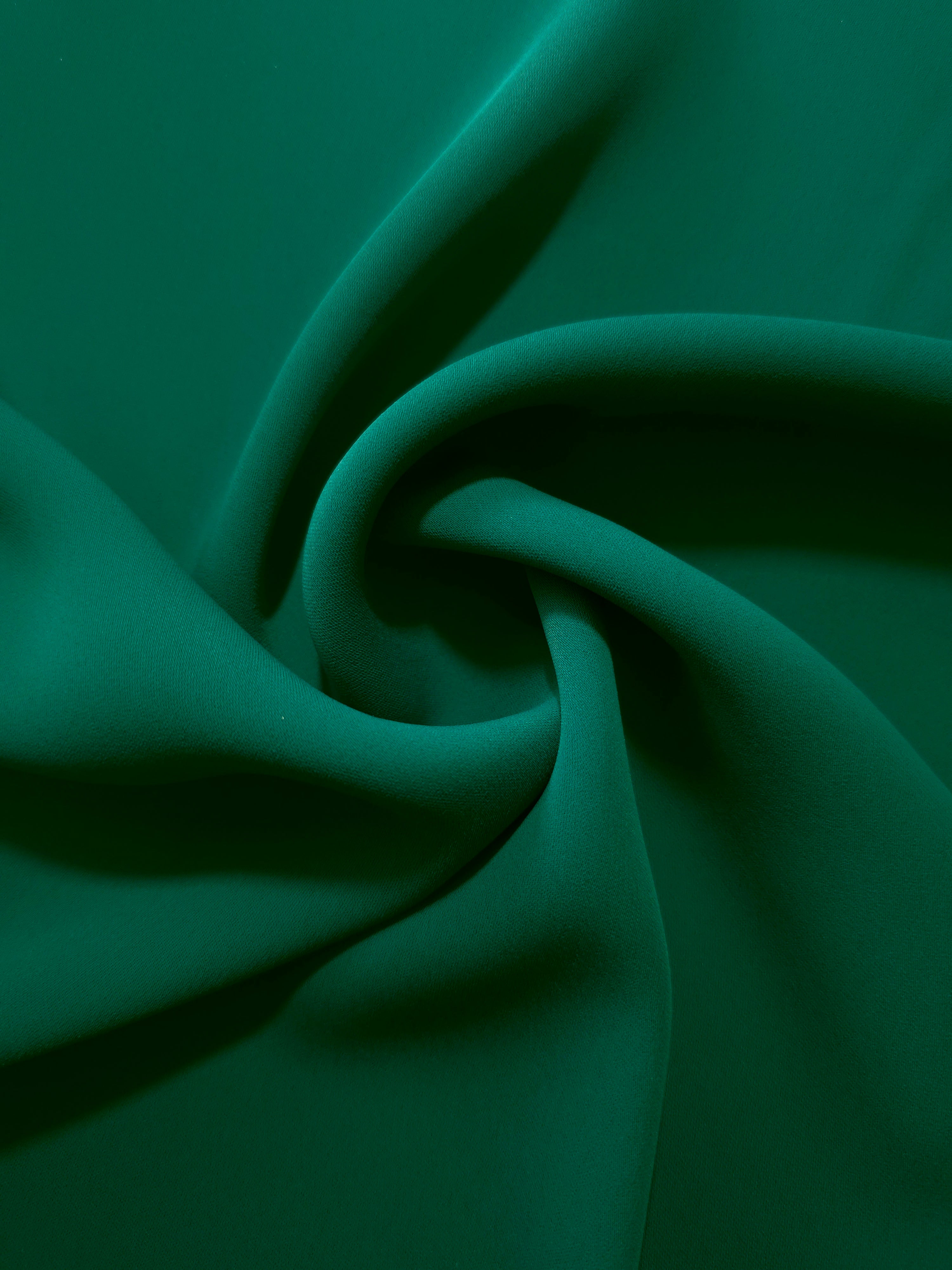 Deep Jade Green silky-soft polyester crepe styled in a swirl to show fluid dressmaking drape and movement