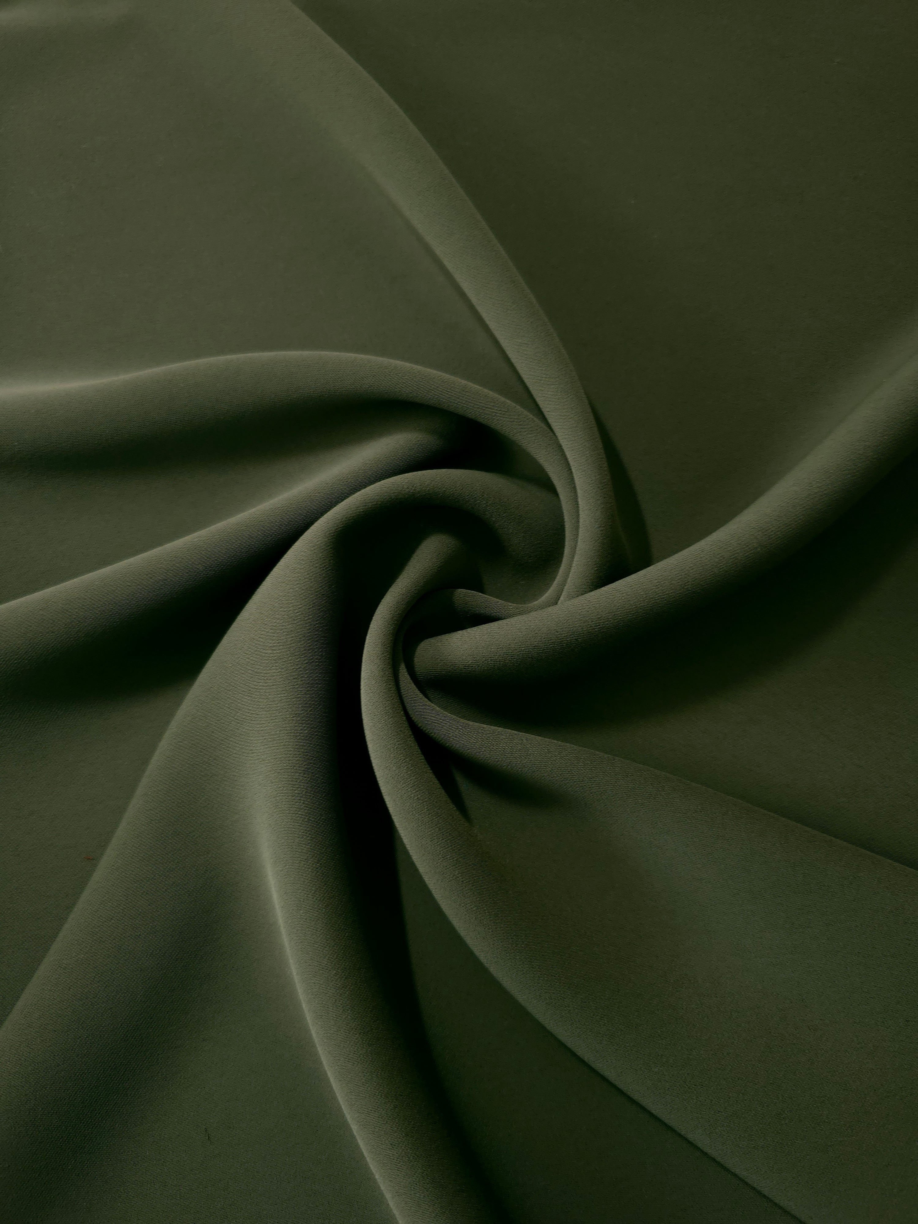 Flowing swirl of Deep Olive Green Korean polyester crepe showing soft drape for blouses, dresses and abayas