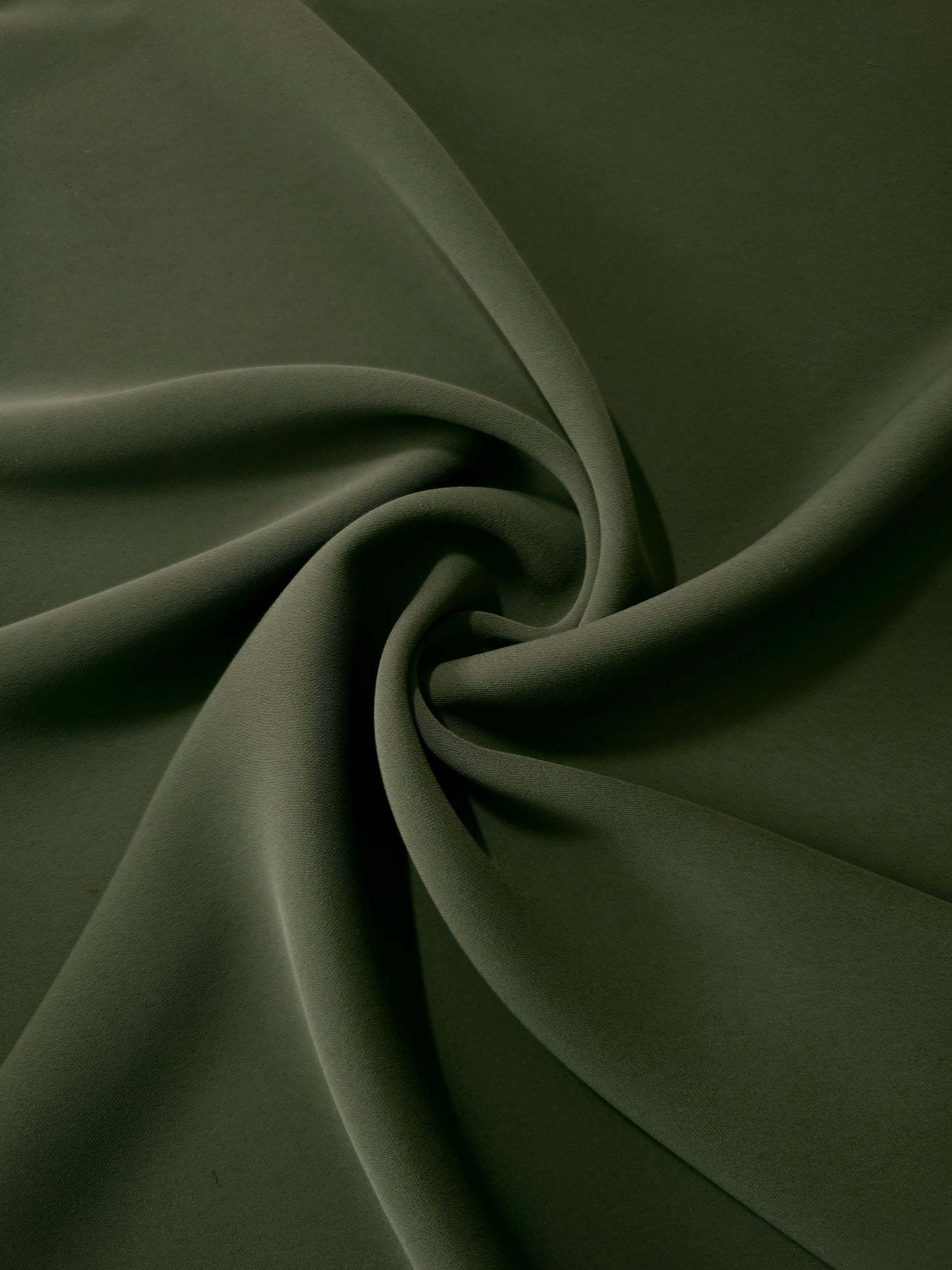 Flowing swirl of Deep Olive Green Korean polyester crepe showing soft drape for blouses, dresses and abayas