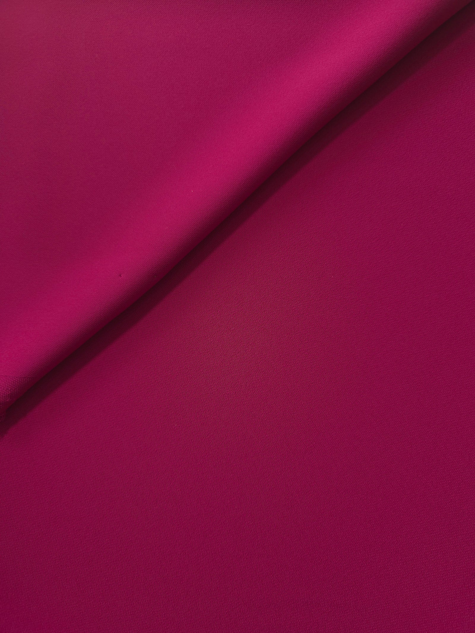 Close-up of Deep Raspberry Pink 100% mechanical polyester crepe showing fine woven texture and a silky-soft hand feel