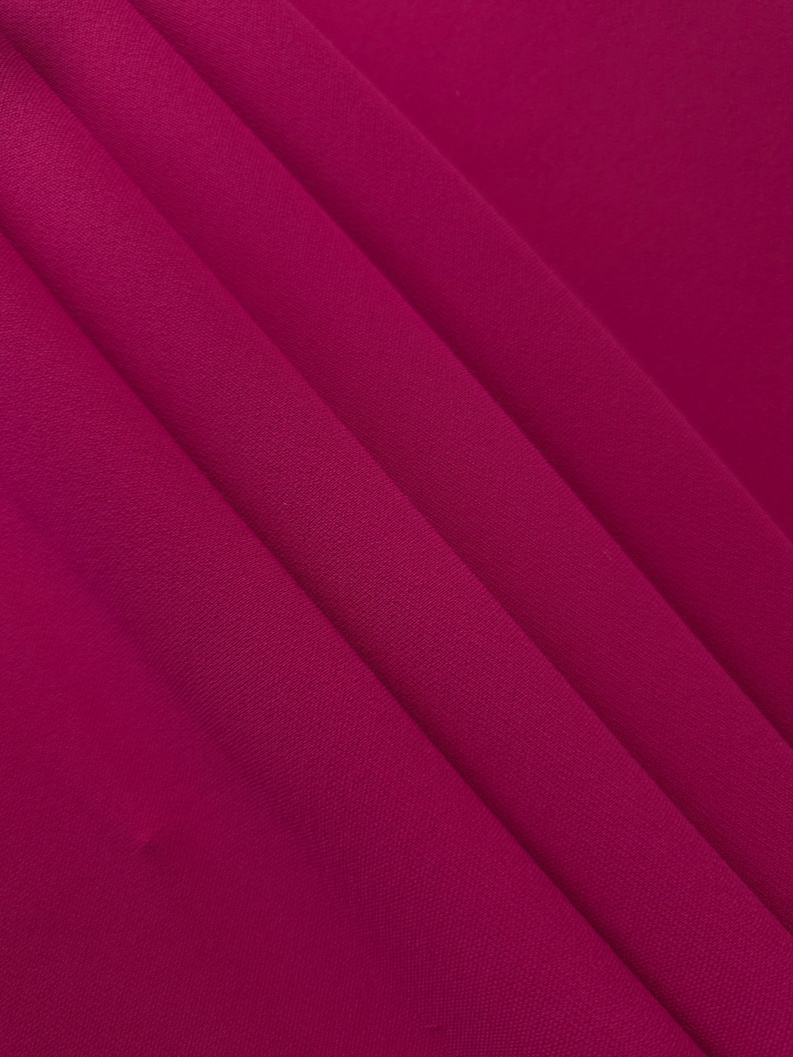 Deep Raspberry Pink polyester crepe arranged in a flowing swirl, showing drape used for abayas and modest fashion