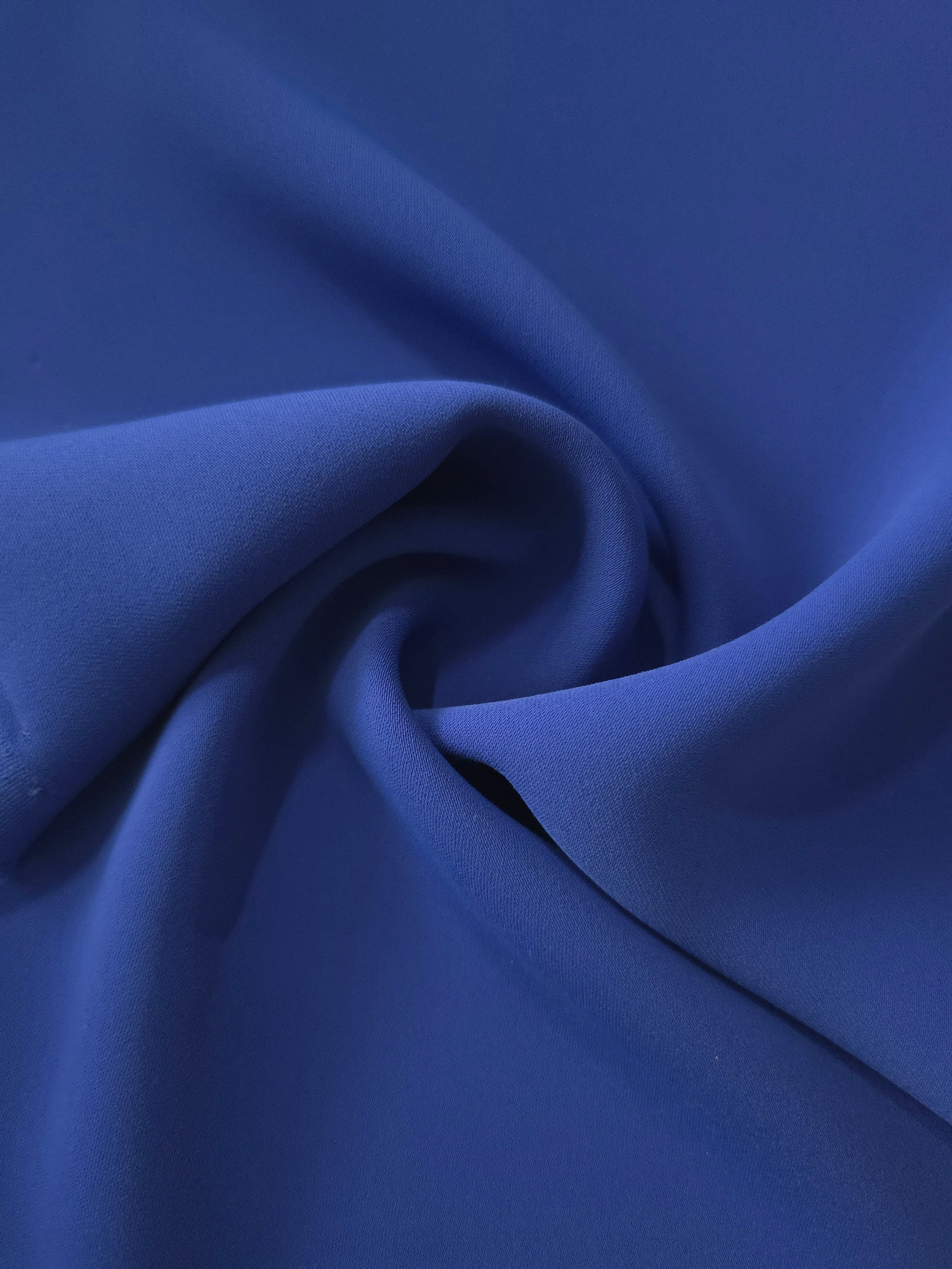 Flowing swirl of Deep Royal Blue polyester crepe showing soft movement for blouses, dresses and abayas