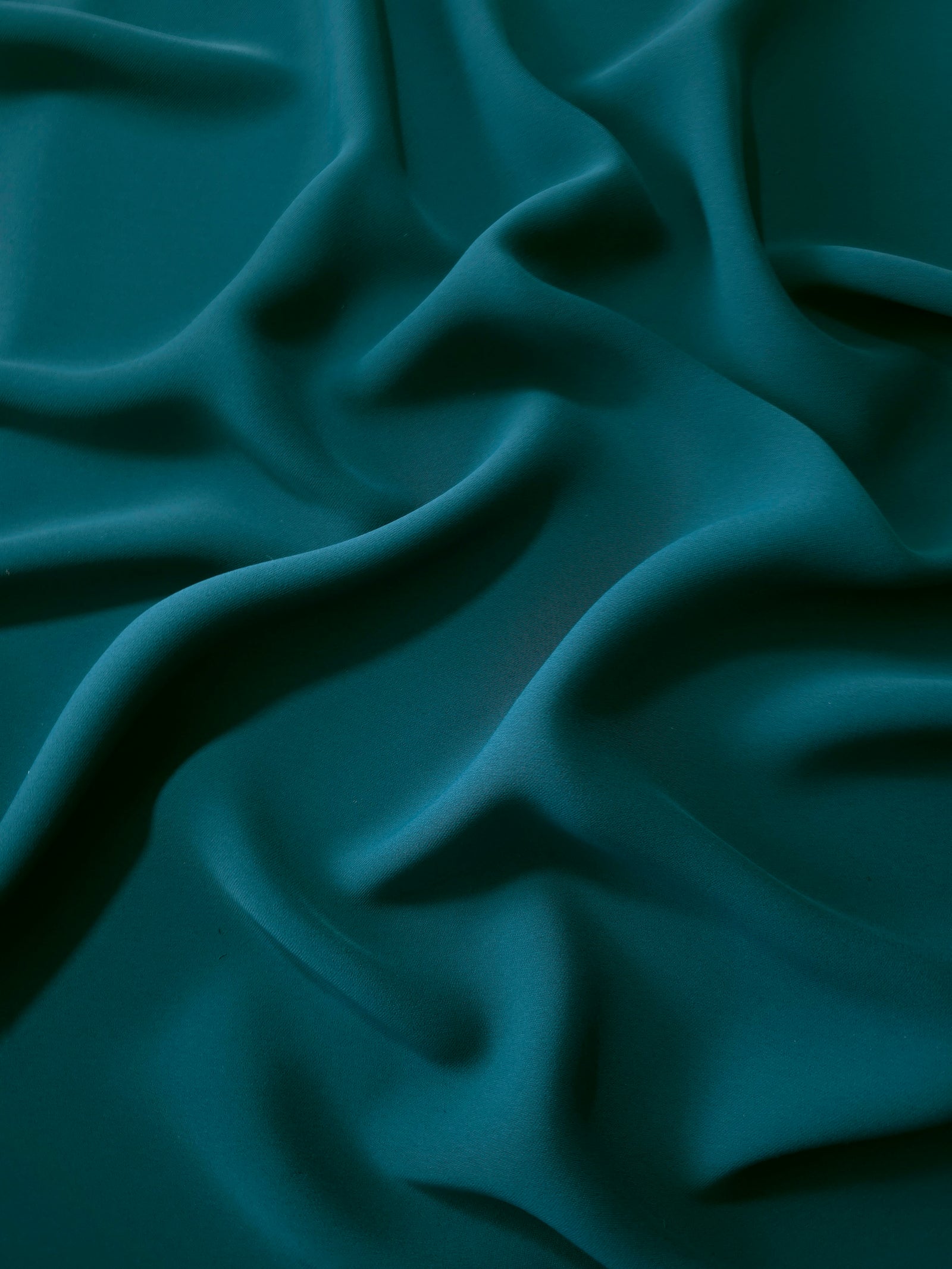 Draped folds of Deep Teal polyester crepe showing opaque coverage and fluid movement for garment making