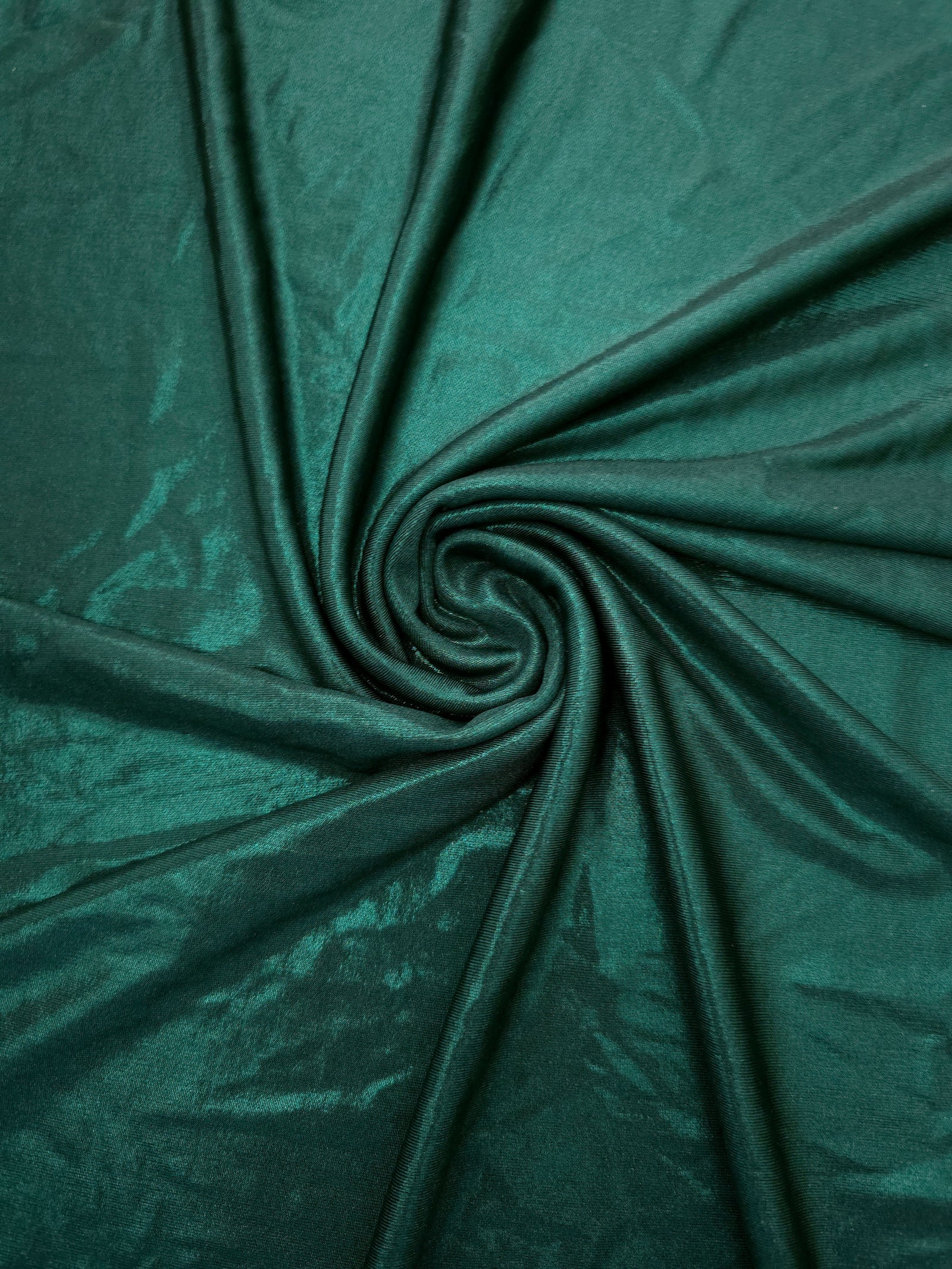Deep Teal Green shimmer foiled stretch fabric arranged in a swirl, highlighting movement and reflective finish for performancewear