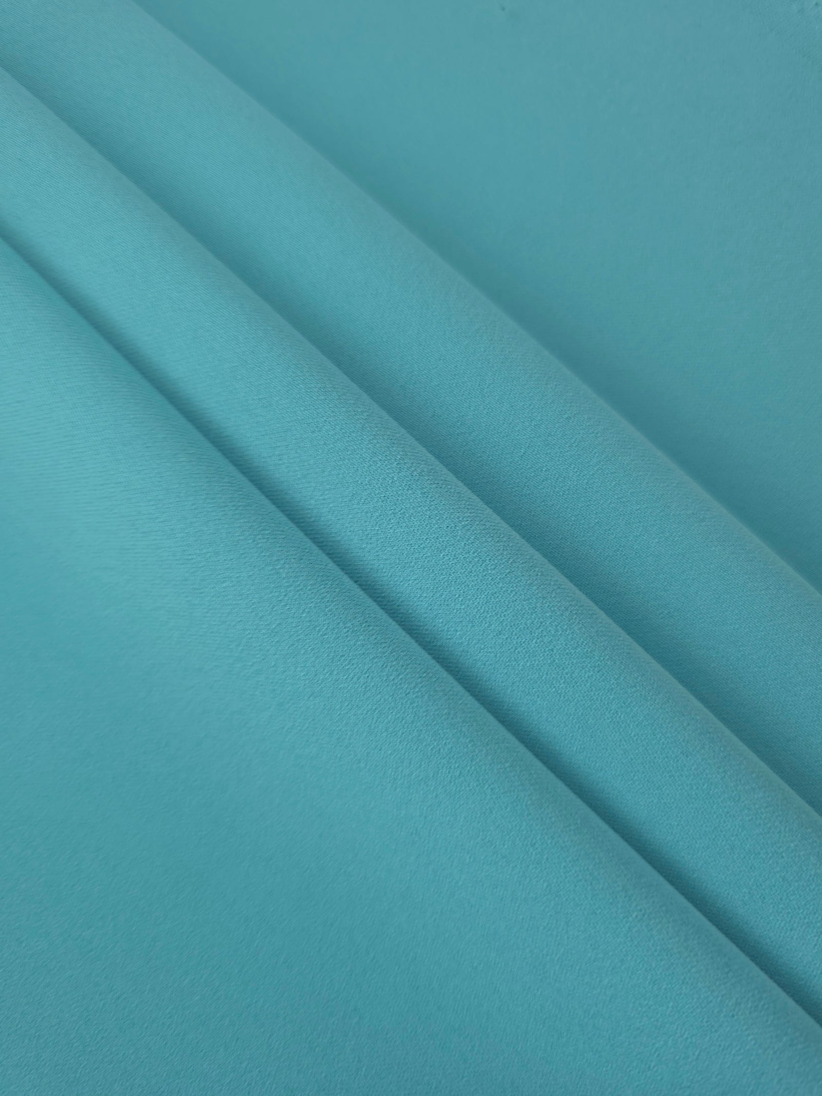 Layered Dusty Aqua Blue polyester crepe showing soft body and slight mechanical stretch for light tailoring