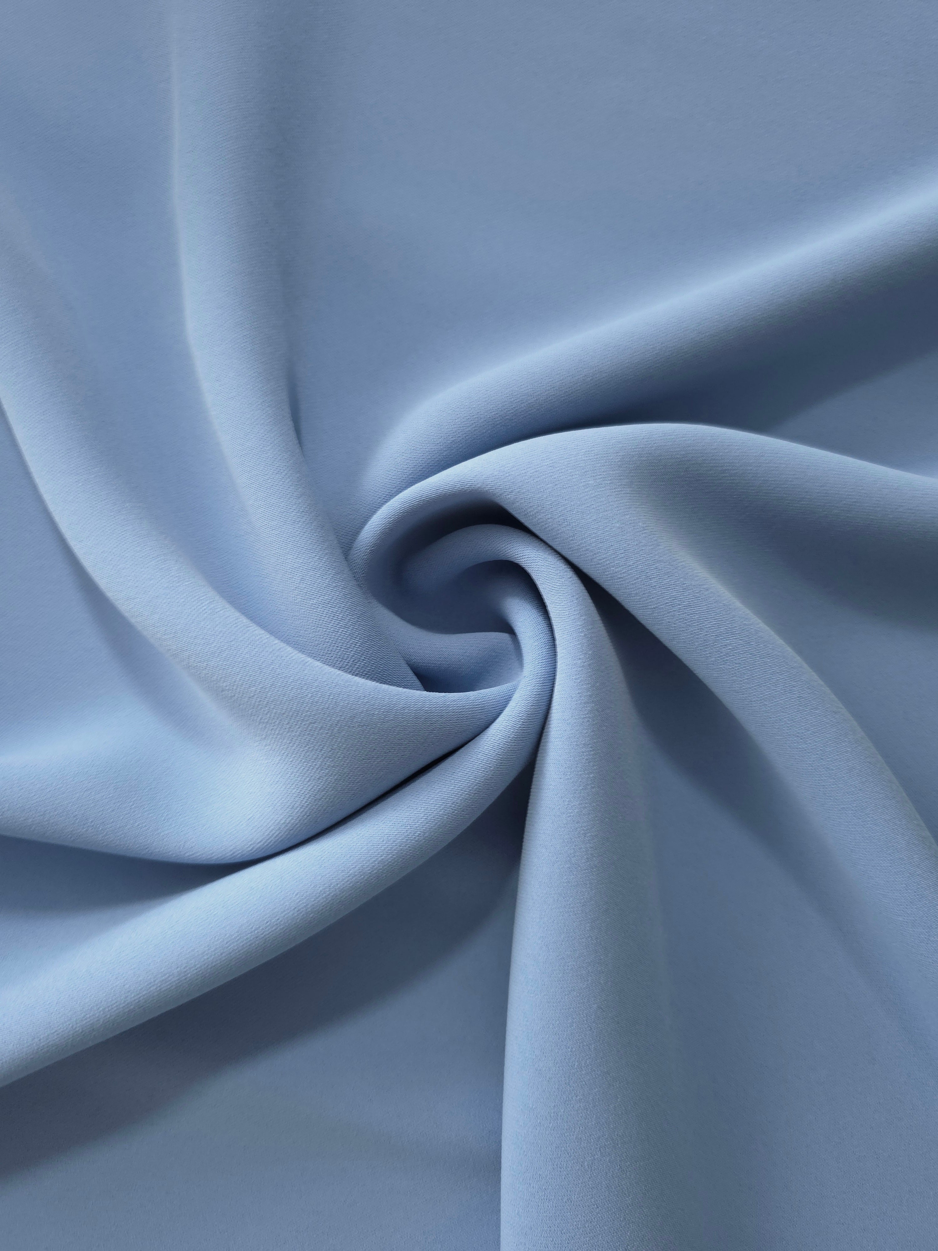 Dusty Denim Blue polyester crepe in a spiral drape, showing flowing form for dresses and modest garments
