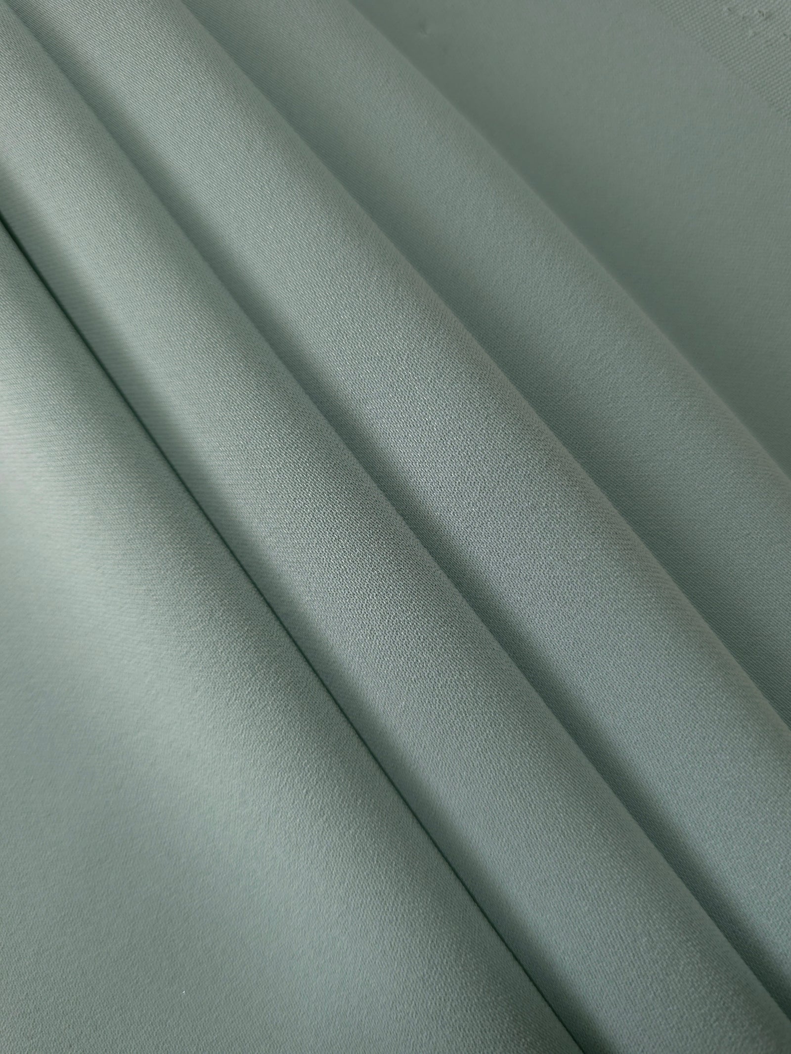 Layered Dusty Eucalyptus Green mechanical polyester crepe showing soft structure and slight mechanical stretch for tailoring