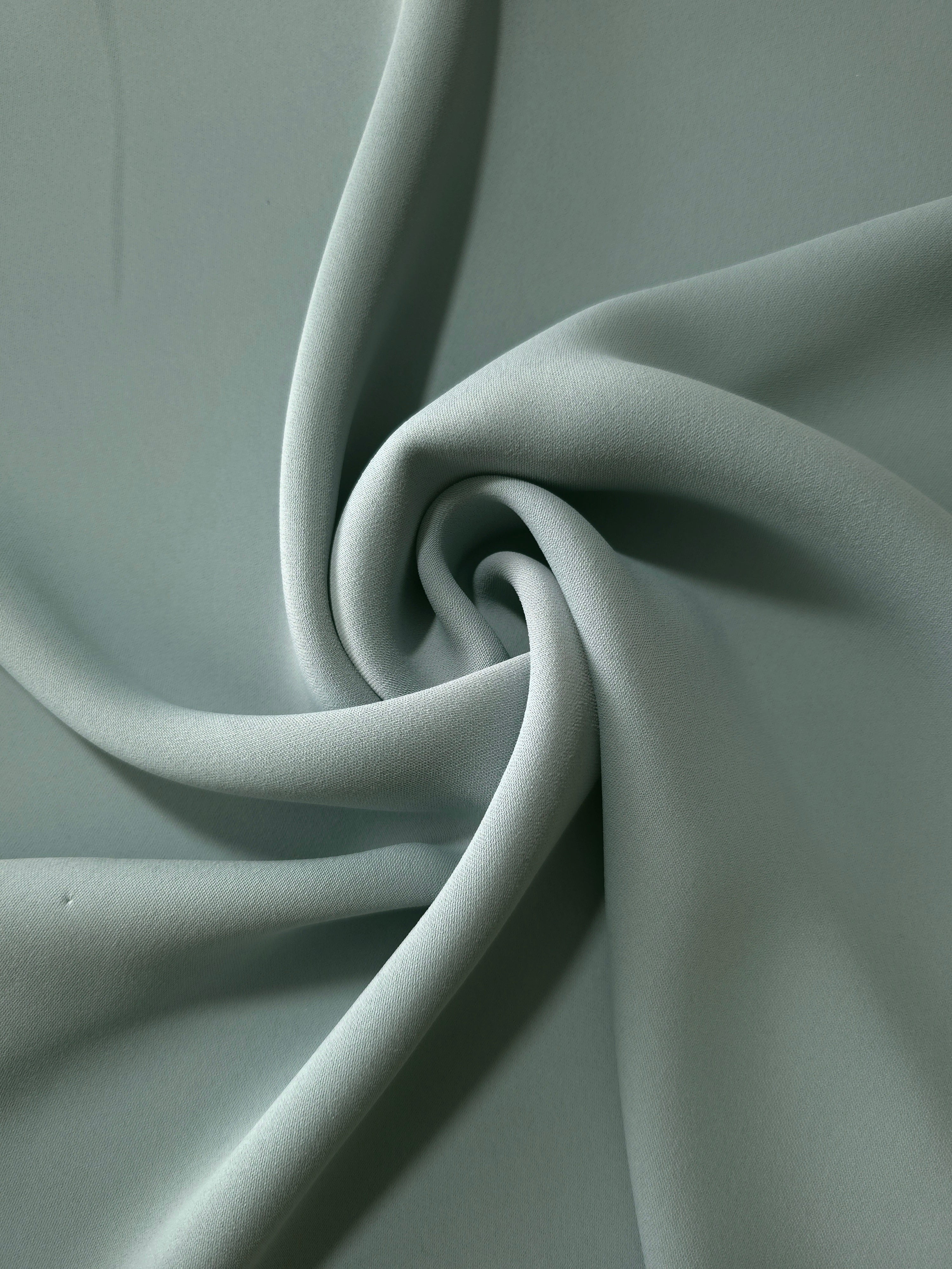Dusty Eucalyptus Green polyester crepe arranged in a flowing swirl, showing drape used for abayas and modest fashion