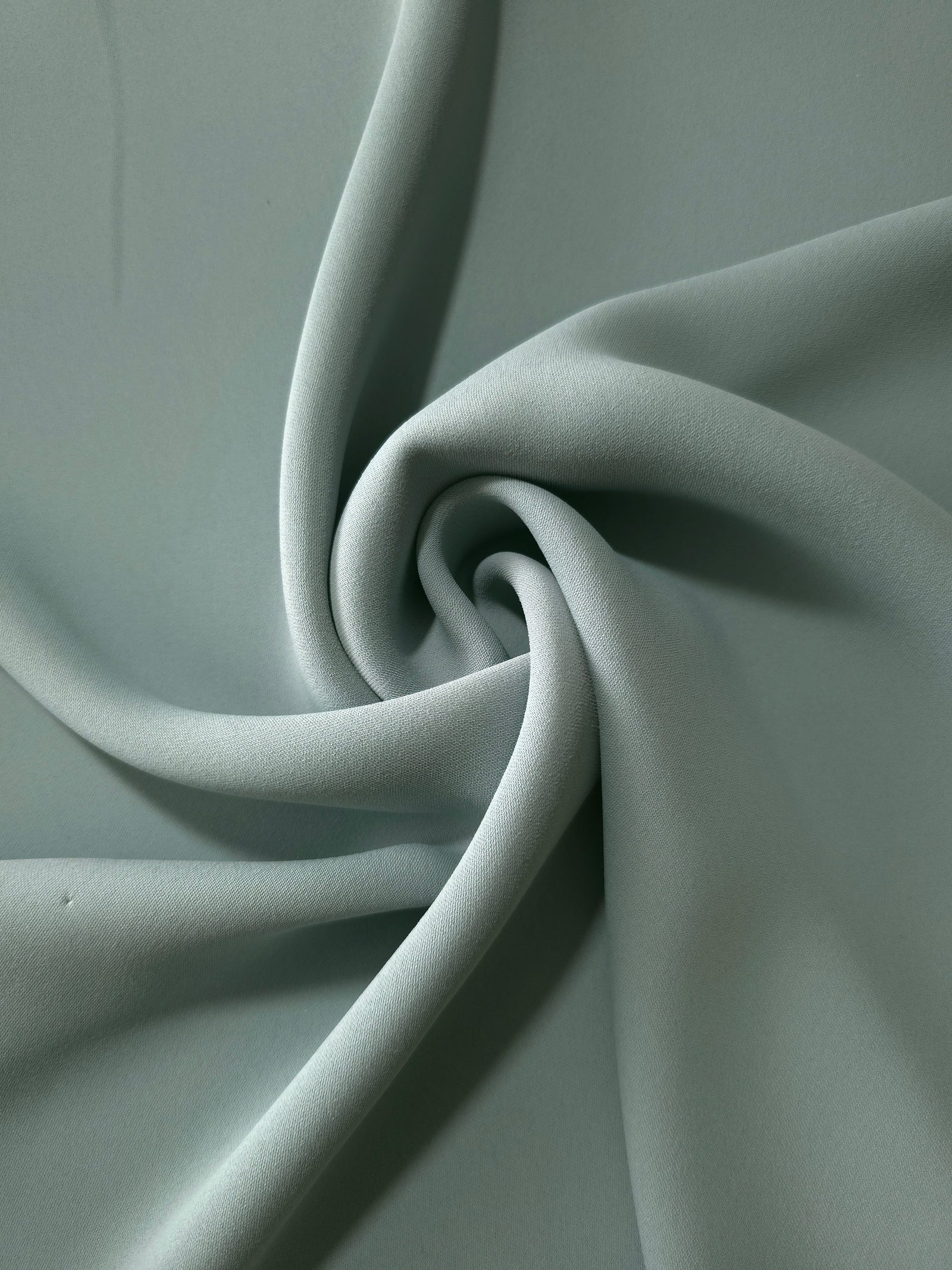 Dusty Eucalyptus Green polyester crepe arranged in a flowing swirl, showing drape used for abayas and modest fashion
