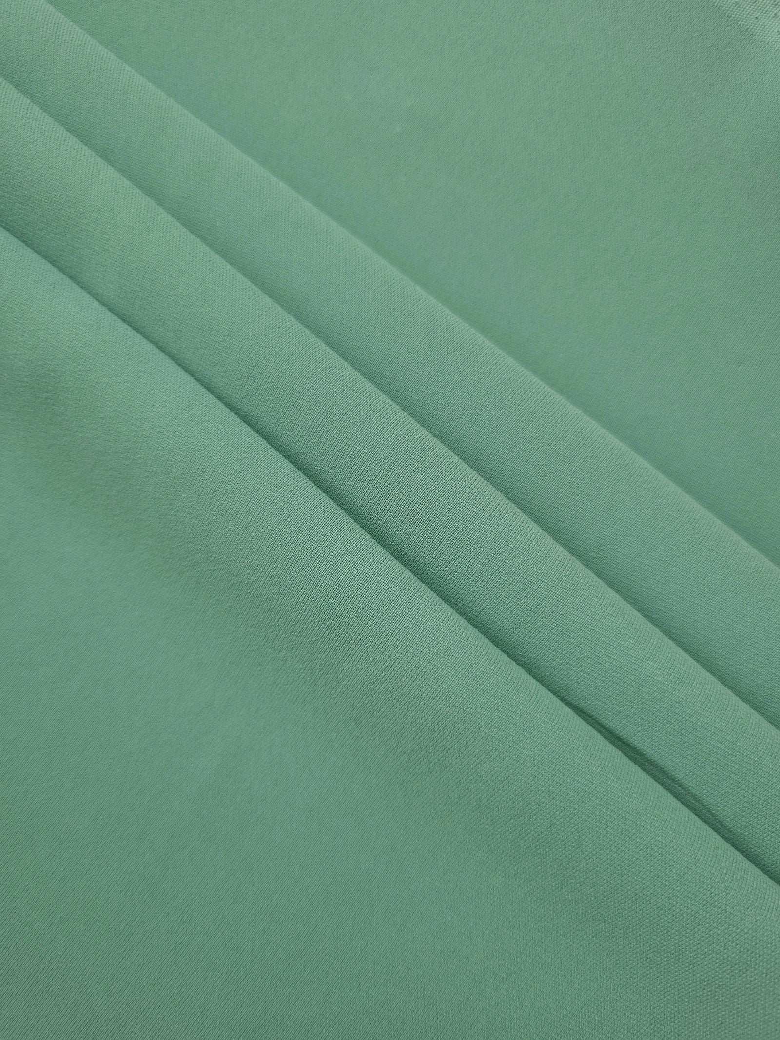 Dusty Mint Green mechanical polyester crepe in layered folds, showing gentle stretch and structure for dressmaking
