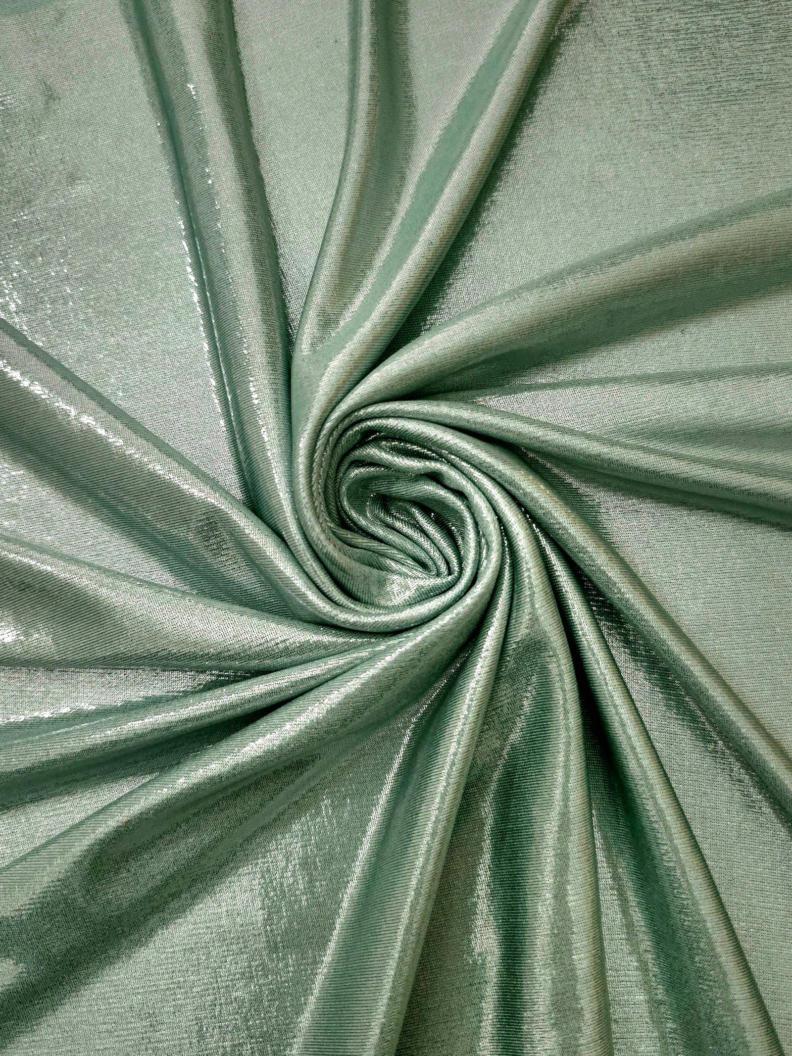 Dusty Sage Green shimmer foiled stretch fabric arranged in a swirl, highlighting movement and reflective finish for performancewear