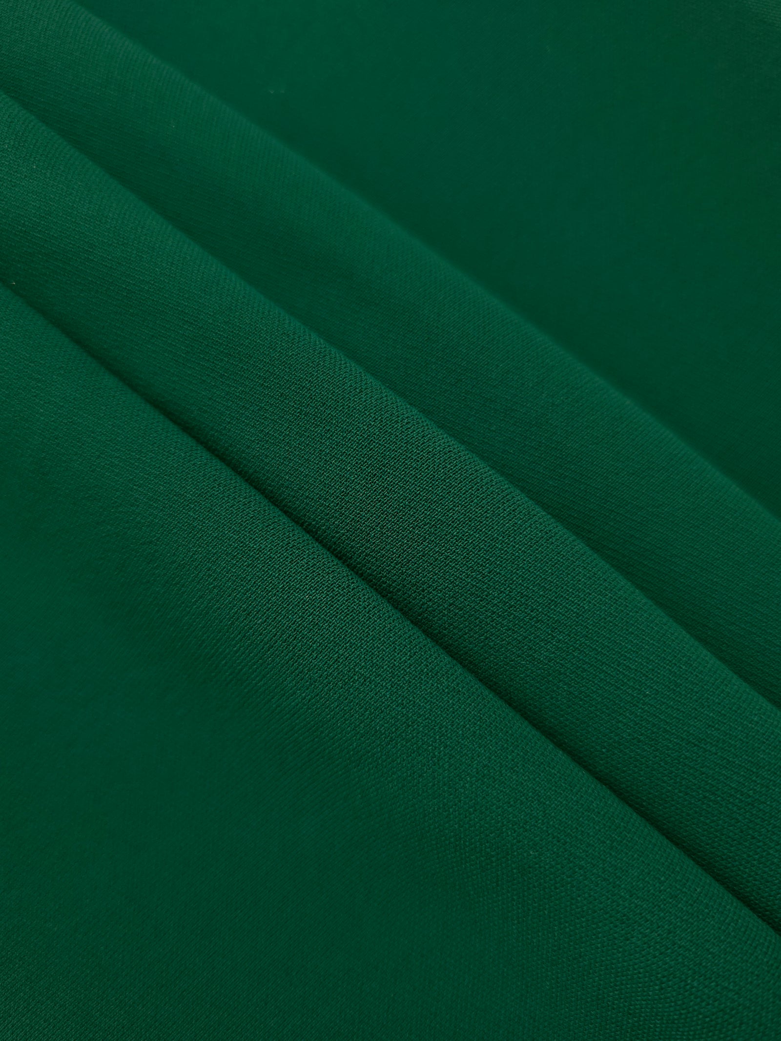Forest Green mechanical polyester crepe in layered folds, showing gentle stretch and structure for dressmaking