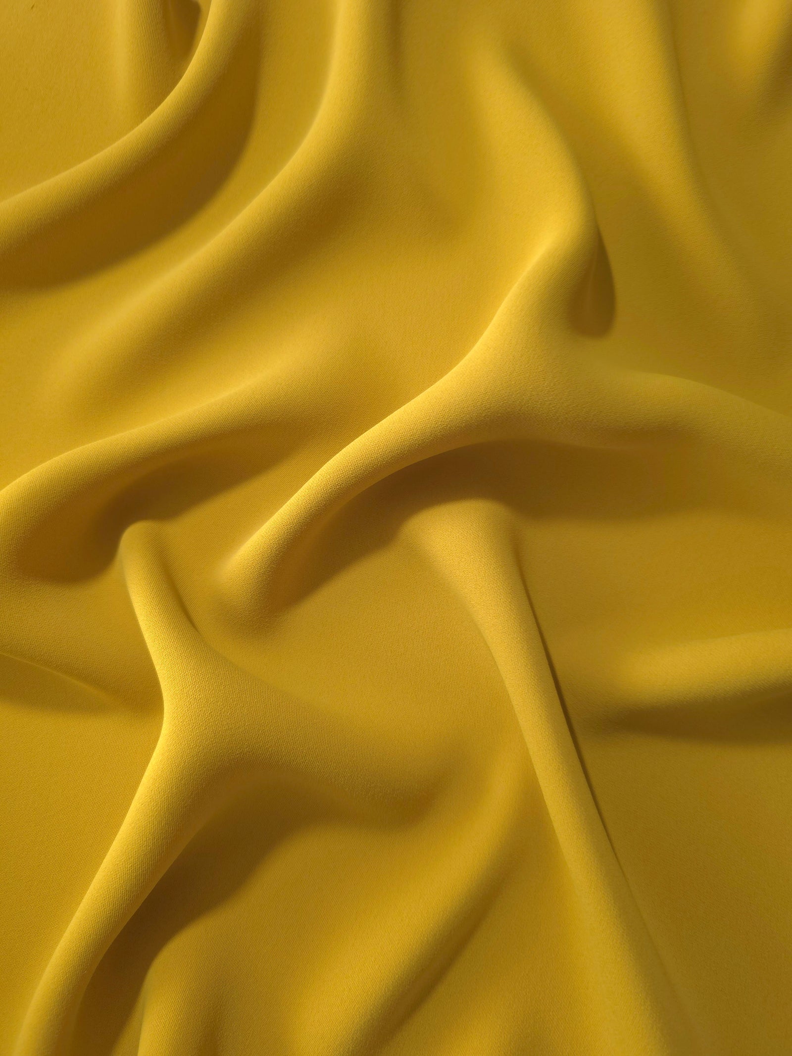 Draped folds of Golden Ochre polyester crepe showing opaque coverage and fluid movement for garment making