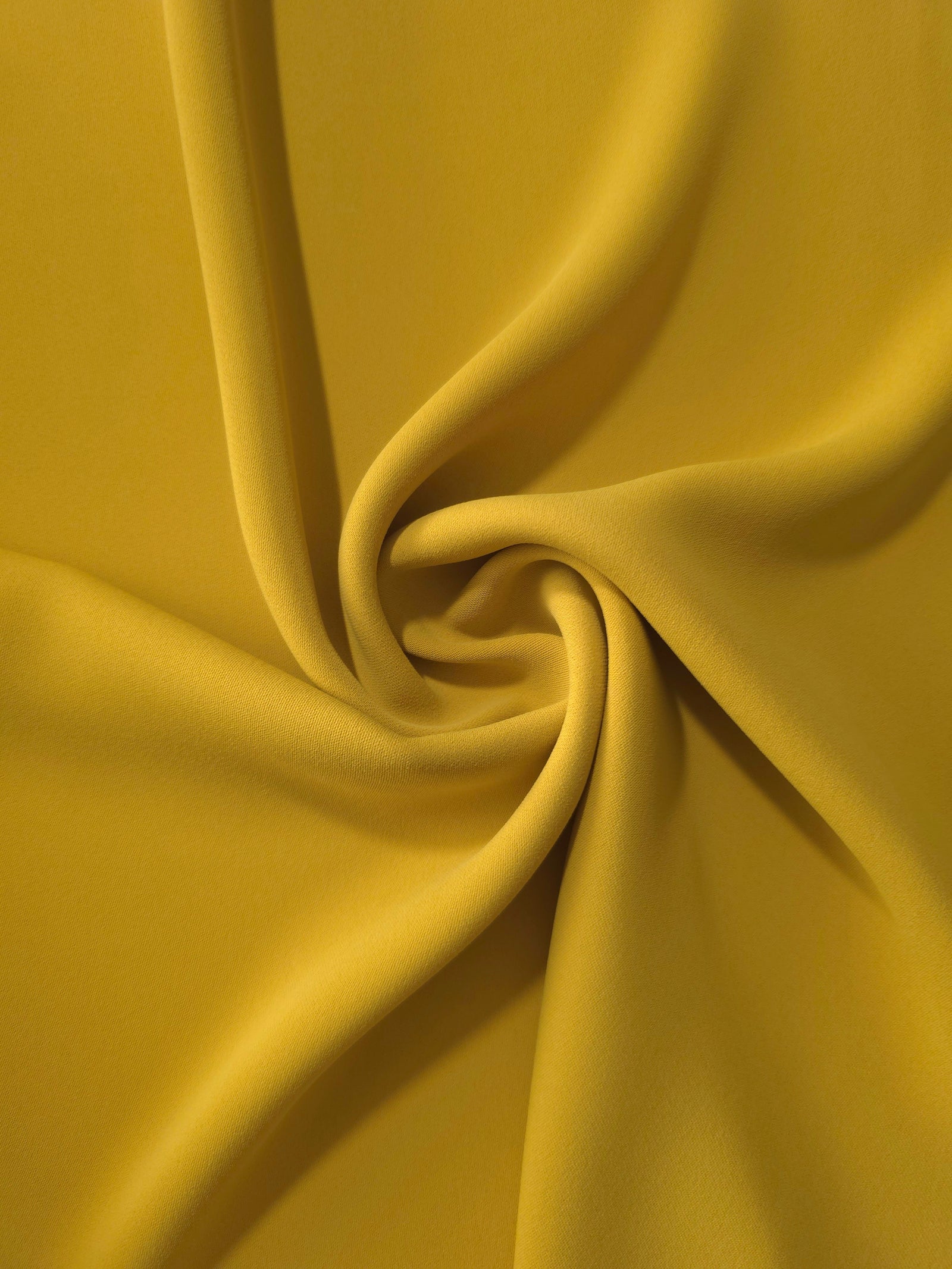 Golden Ochre silky-soft polyester crepe styled in a swirl to show fluid dressmaking drape and movement