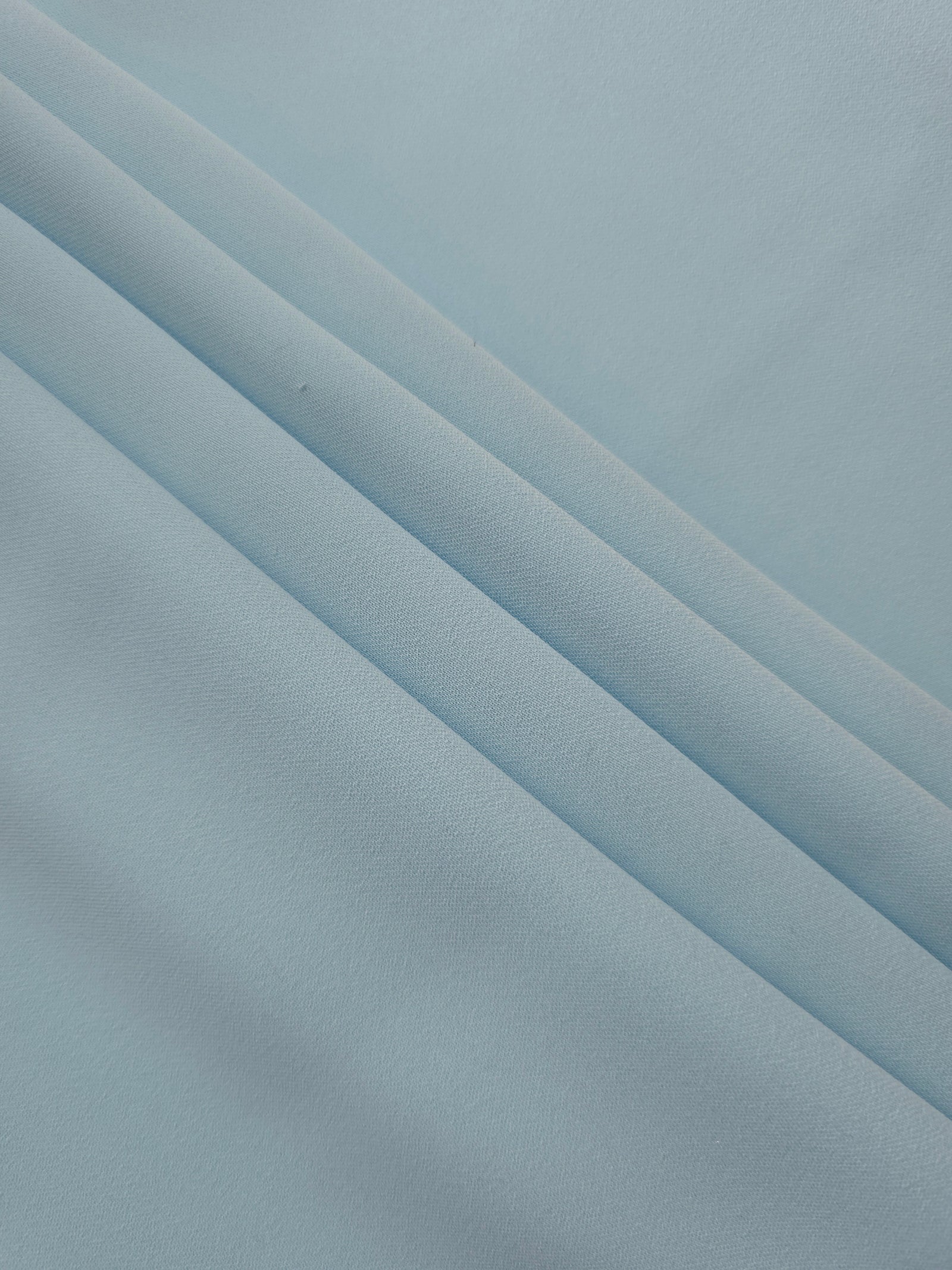 Layered folds of Ice Blue 100% mechanical polyester crepe showing body and gentle construction stretch