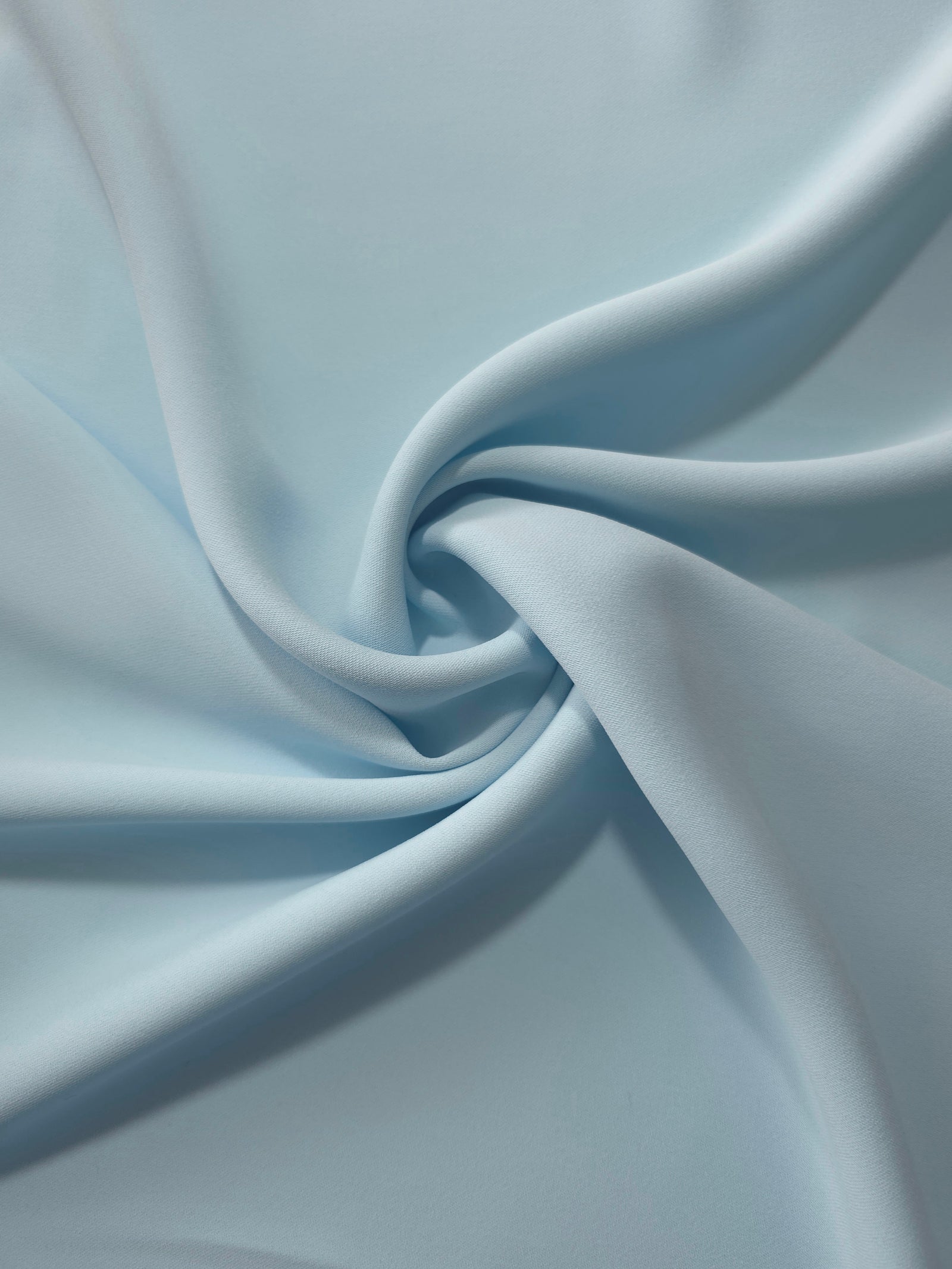 Ice Blue opaque polyester crepe in a spiral drape, showing flowing form for skirts and modest garments