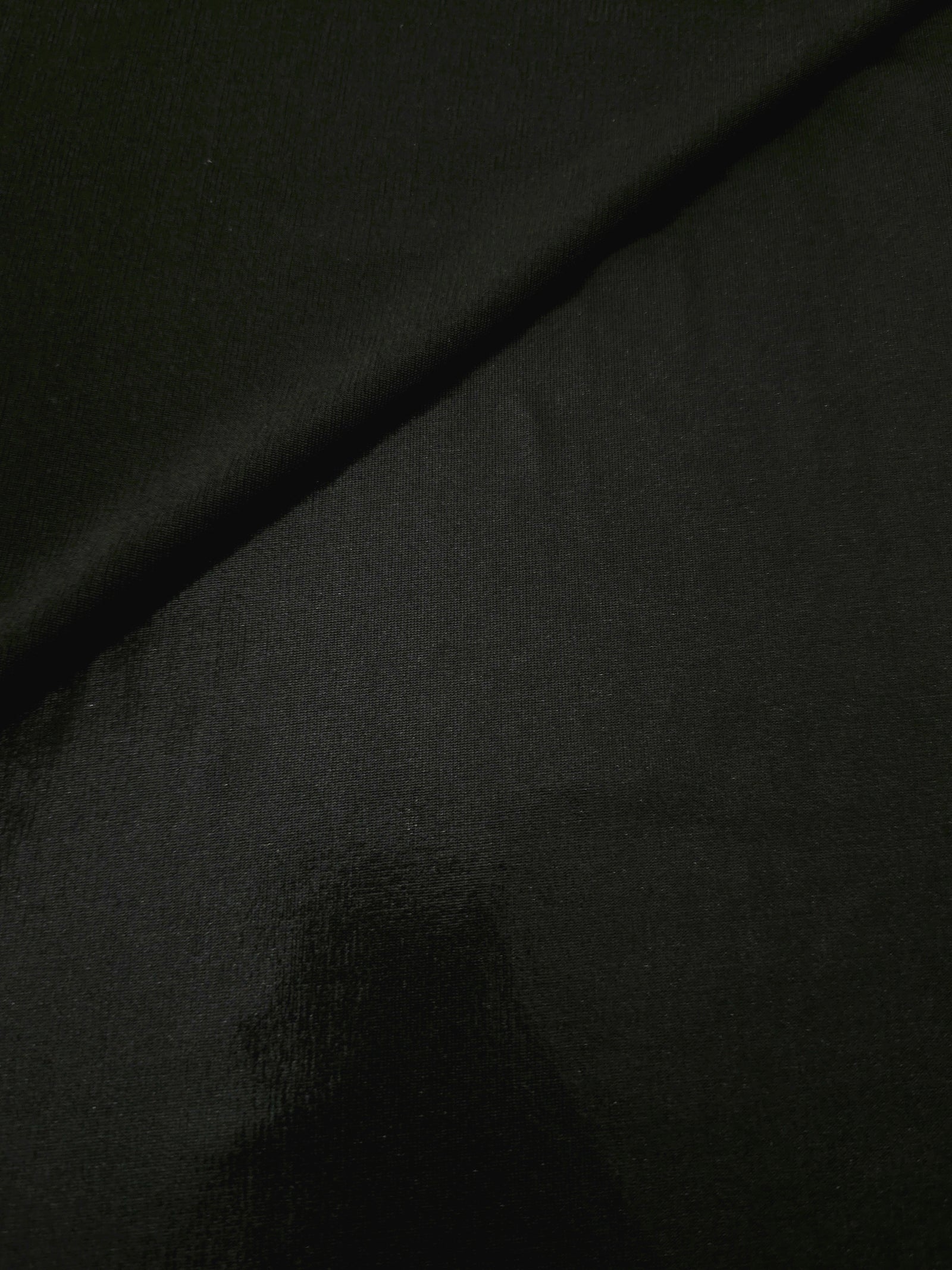 Soft fold of Jet Black metallic foiled spandex highlighting reflective sheen and supple movement for dresses and stagewear