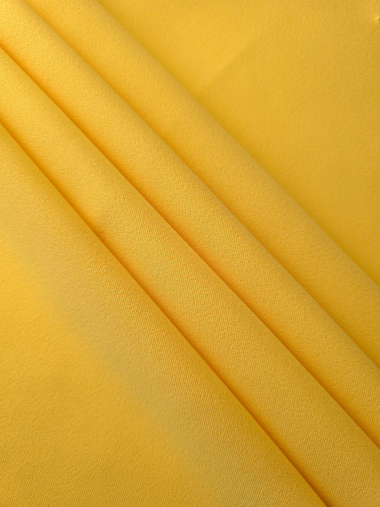 Layered Mustard Yellow mechanical polyester crepe showing soft structure and slight mechanical stretch for tailoring