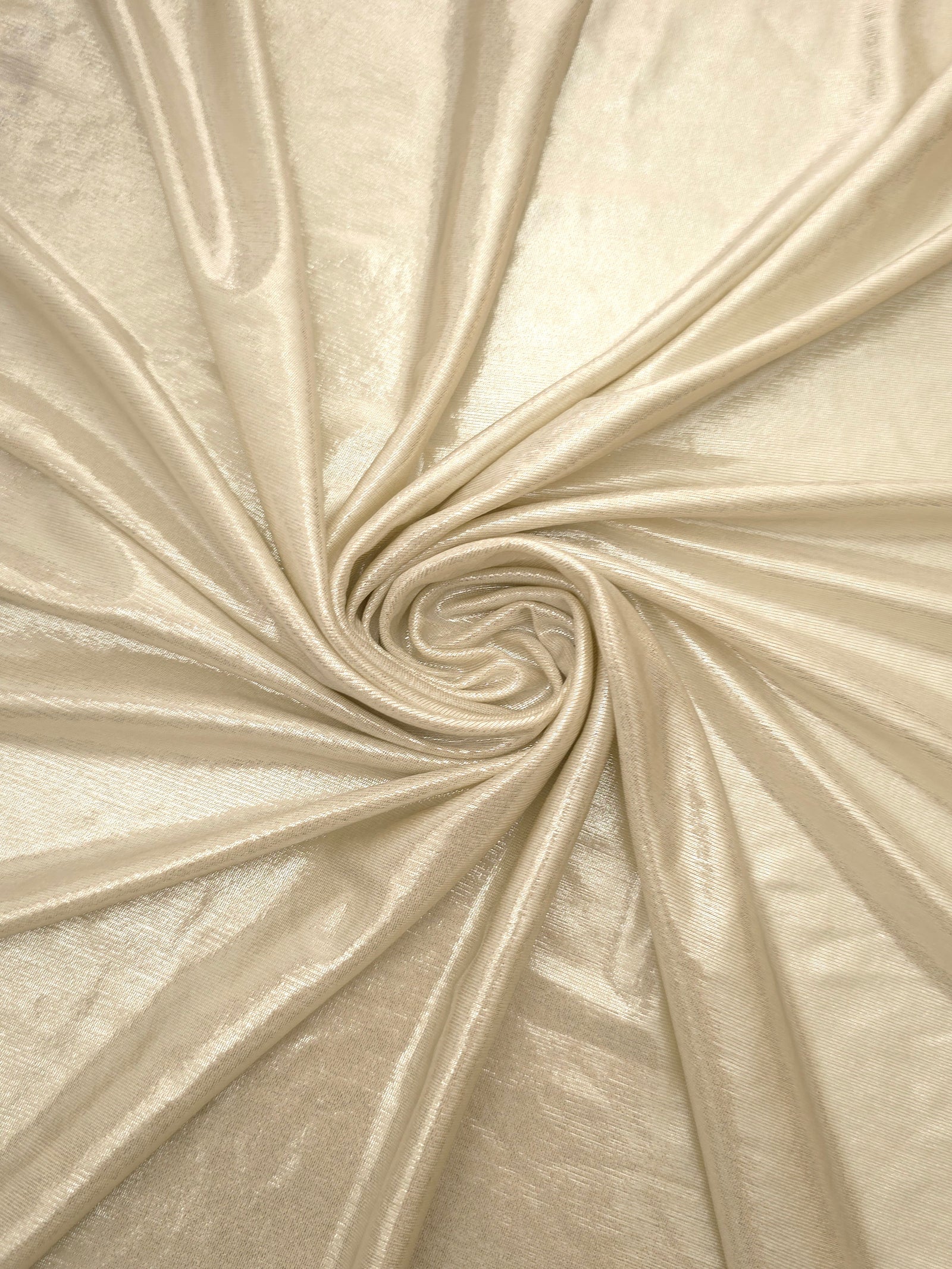 Pale Butter Cream metallic stretch fabric in a flowing swirl, emphasizing foil shimmer and drape for partywear and statement fashion