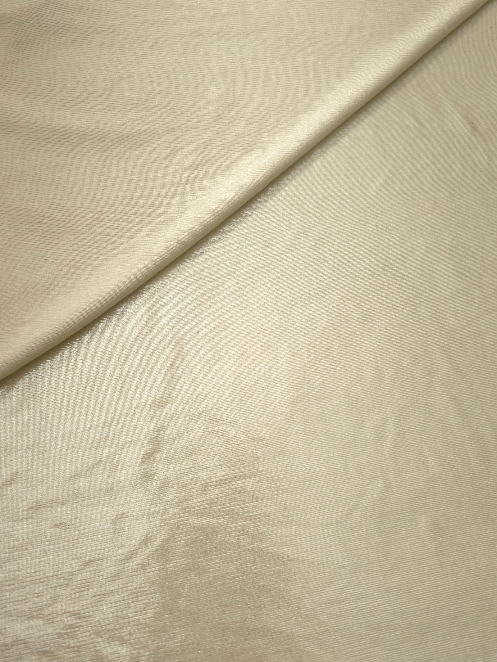 Pale Butter Cream foiled stretch fabric in a gentle fold, showing metallic shimmer and flexibility for partywear and performance fashion