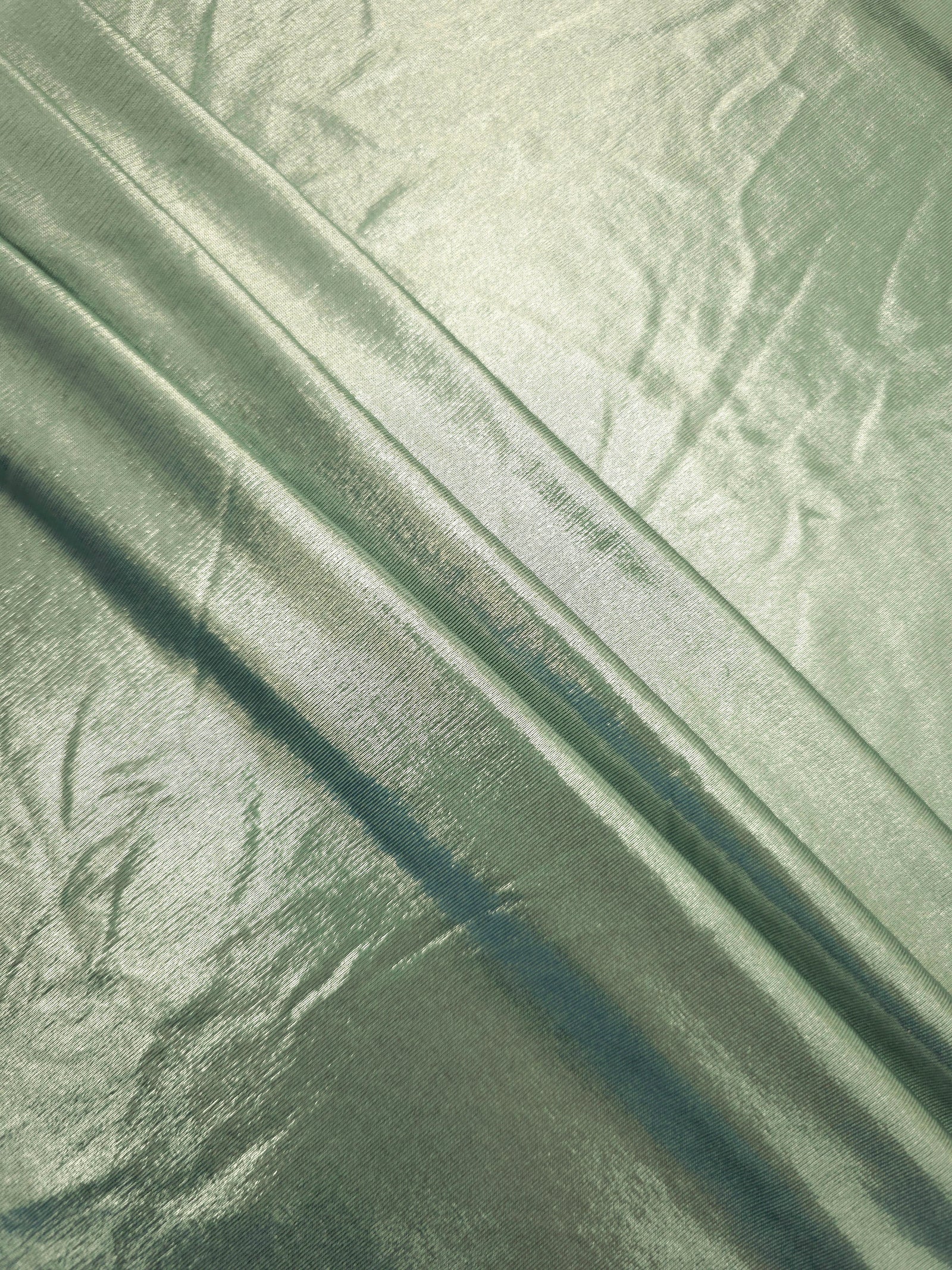 Layered Pale Sage Green metallic stretch fabric with reflective foil finish, showing flexible body for dancewear and occasion fashion