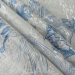 Blue palm vine linen-look jacquard fabric folded view showing apparel drape and woven design.