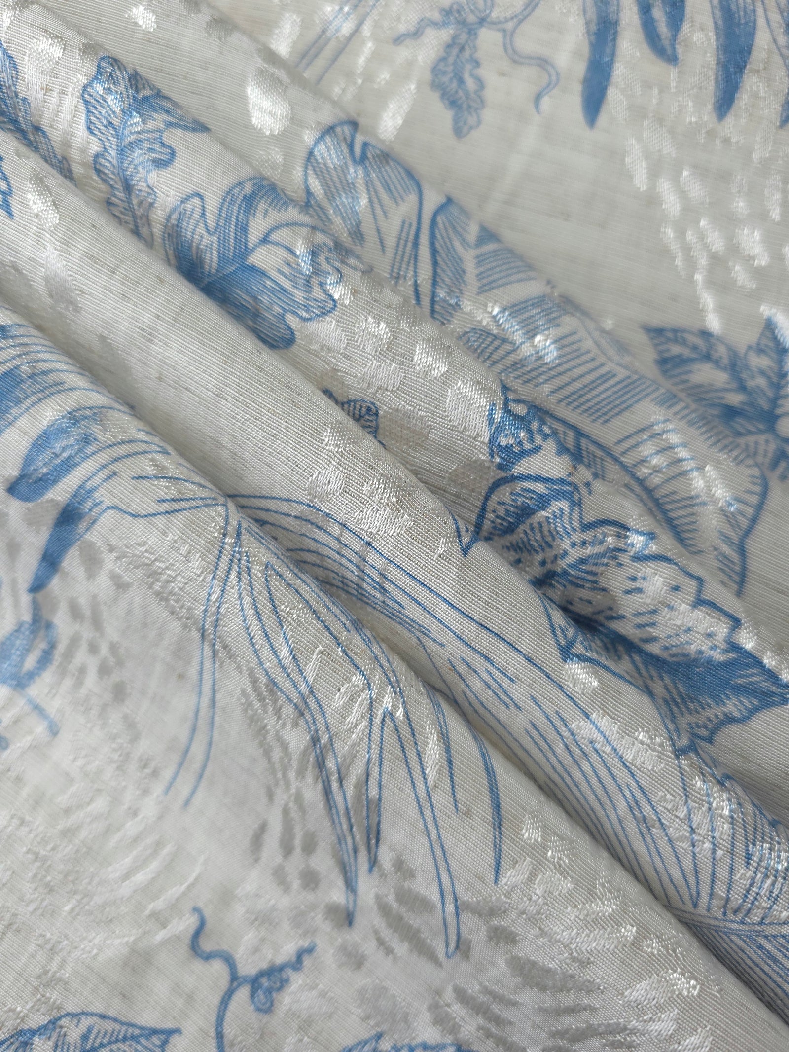 Blue palm vine linen-look jacquard fabric folded view showing apparel drape and woven design.