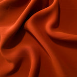 Rust Orange Korean polyester dress fabric shown in draped folds for occasionwear, blouses and dresses
