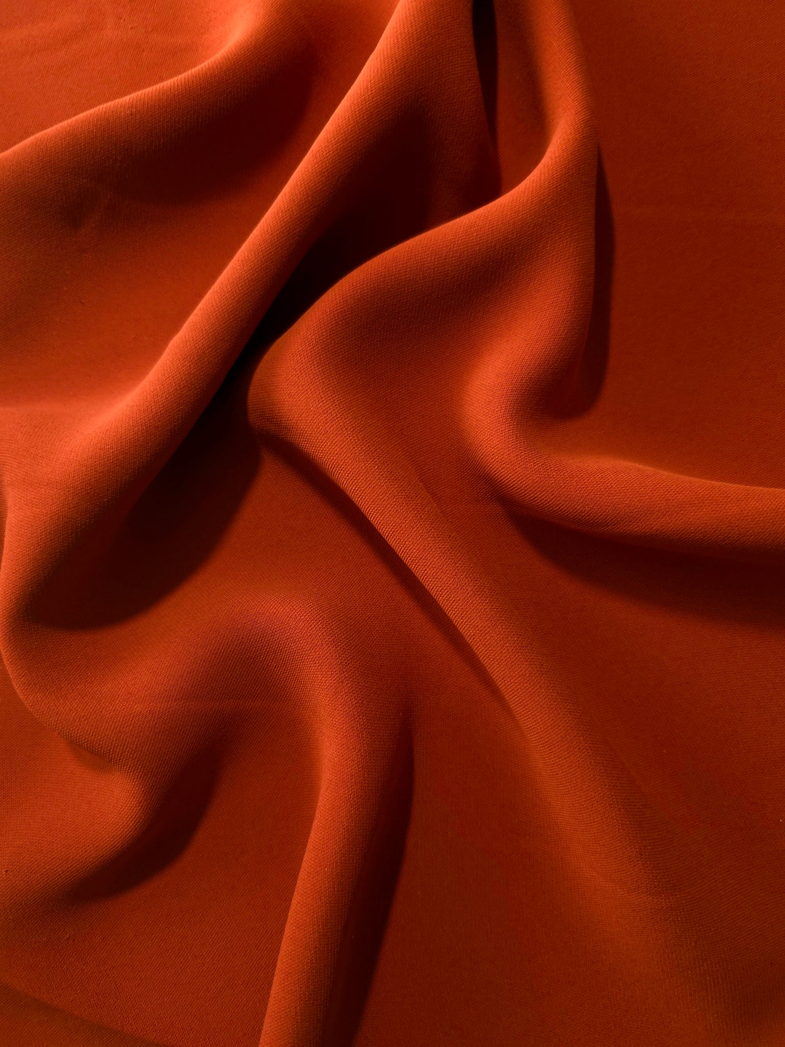 Rust Orange Korean polyester dress fabric shown in draped folds for occasionwear, blouses and dresses