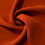 Flowing swirl of Rust Orange Korean polyester crepe showing soft drape for blouses, dresses and abayas