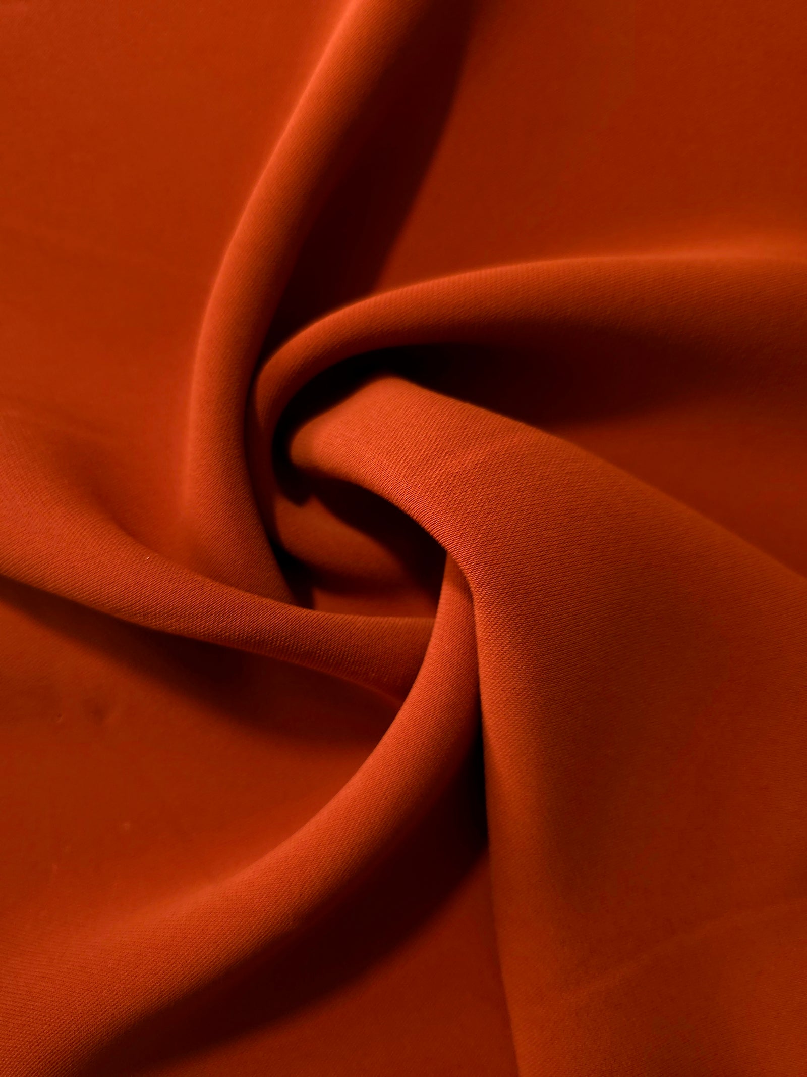 Flowing swirl of Rust Orange Korean polyester crepe showing soft drape for blouses, dresses and abayas