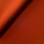 Loose fold of Rust Orange polyester crepe showing smooth fluid drape for dresses, skirts and soft tailoring