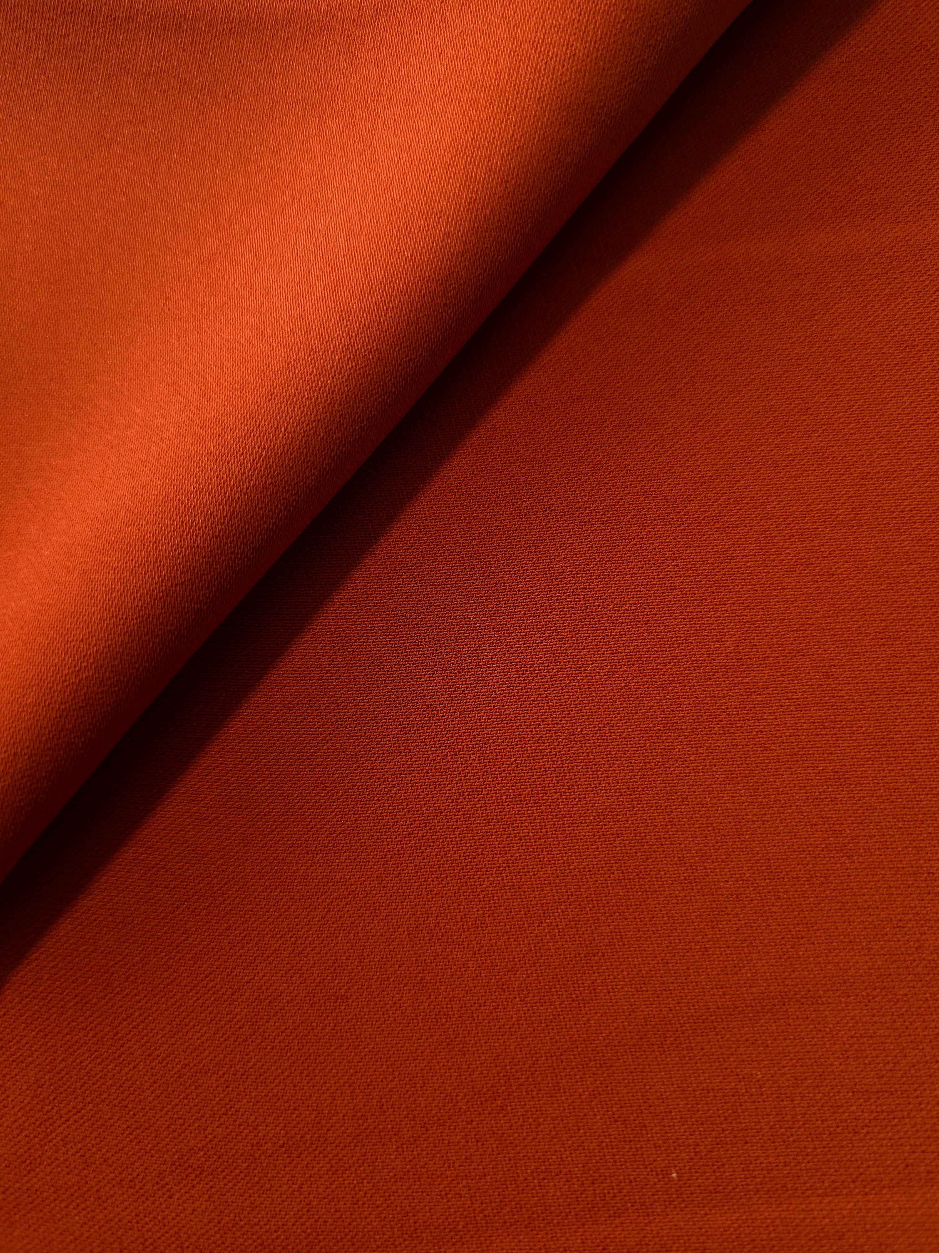 Loose fold of Rust Orange polyester crepe showing smooth fluid drape for dresses, skirts and soft tailoring