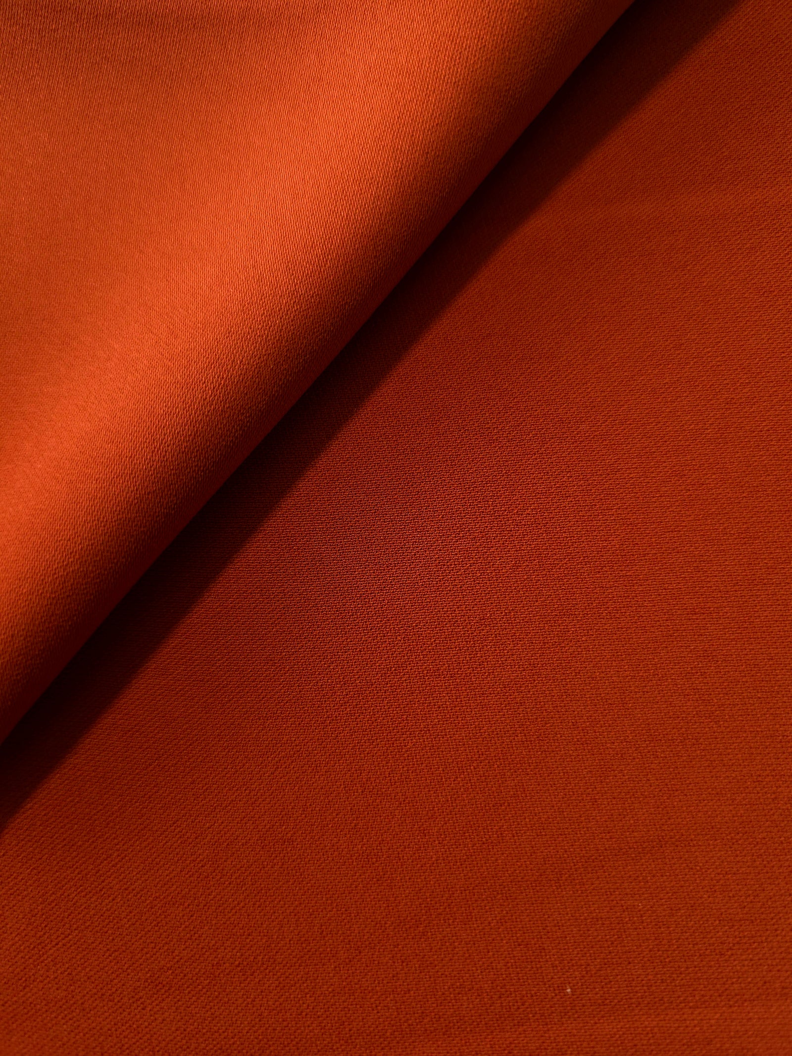 Loose fold of Rust Orange polyester crepe showing smooth fluid drape for dresses, skirts and soft tailoring