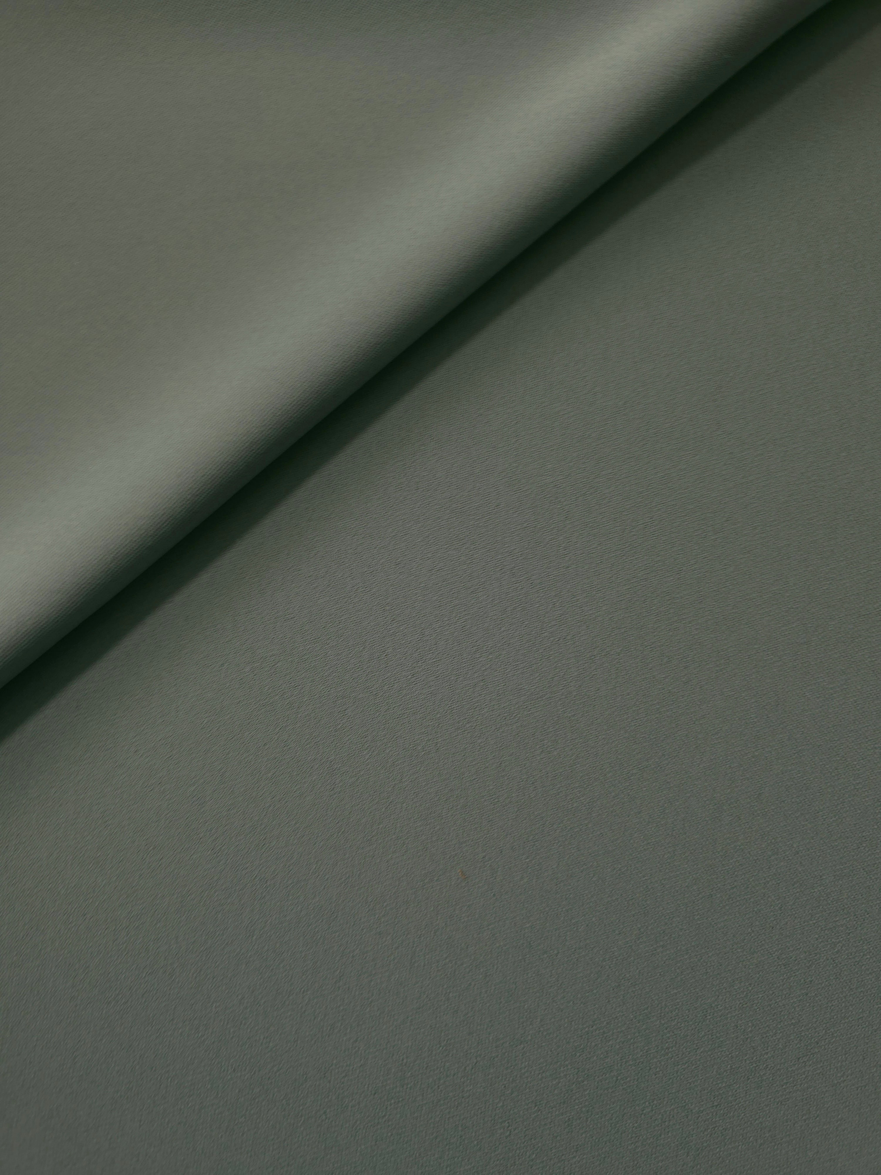 Soft fold of Smoky Sage Green opaque polyester crepe showing fluid dressmaking drape for dresses and skirts