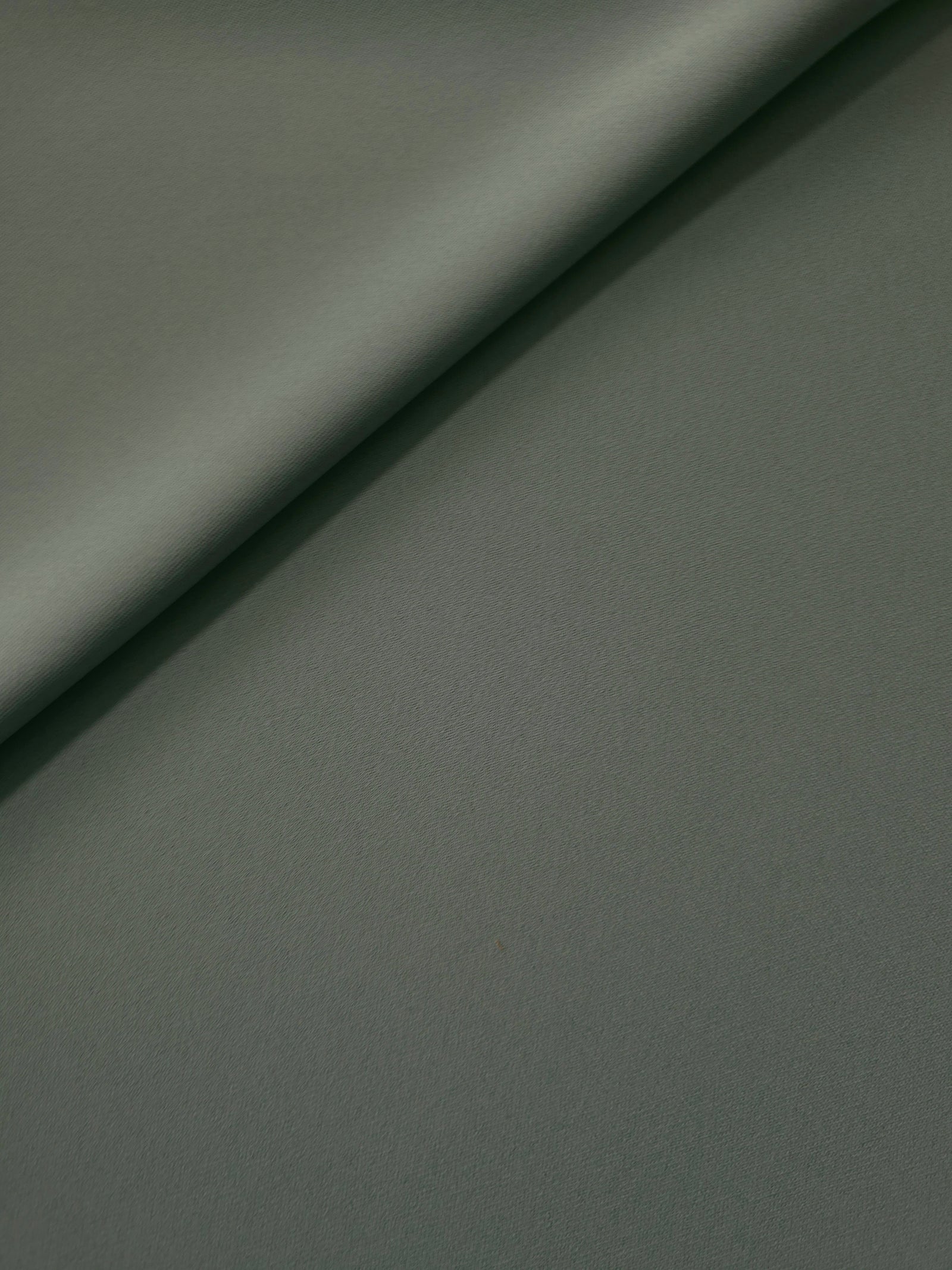 Soft fold of Smoky Sage Green opaque polyester crepe showing fluid dressmaking drape for dresses and skirts