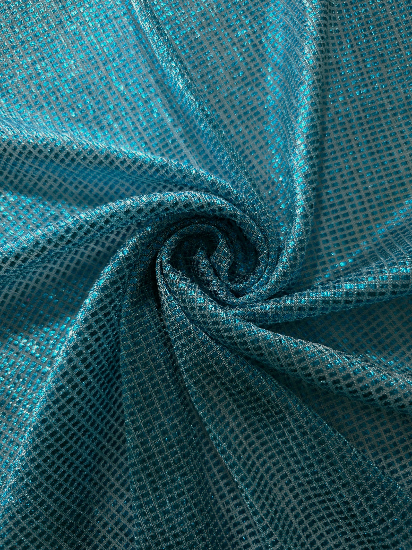 Swirl-draped Aqua Teal Sheer Square Shimmer Stretch Tulle Fabric showing structured square reflections moving through soft folds